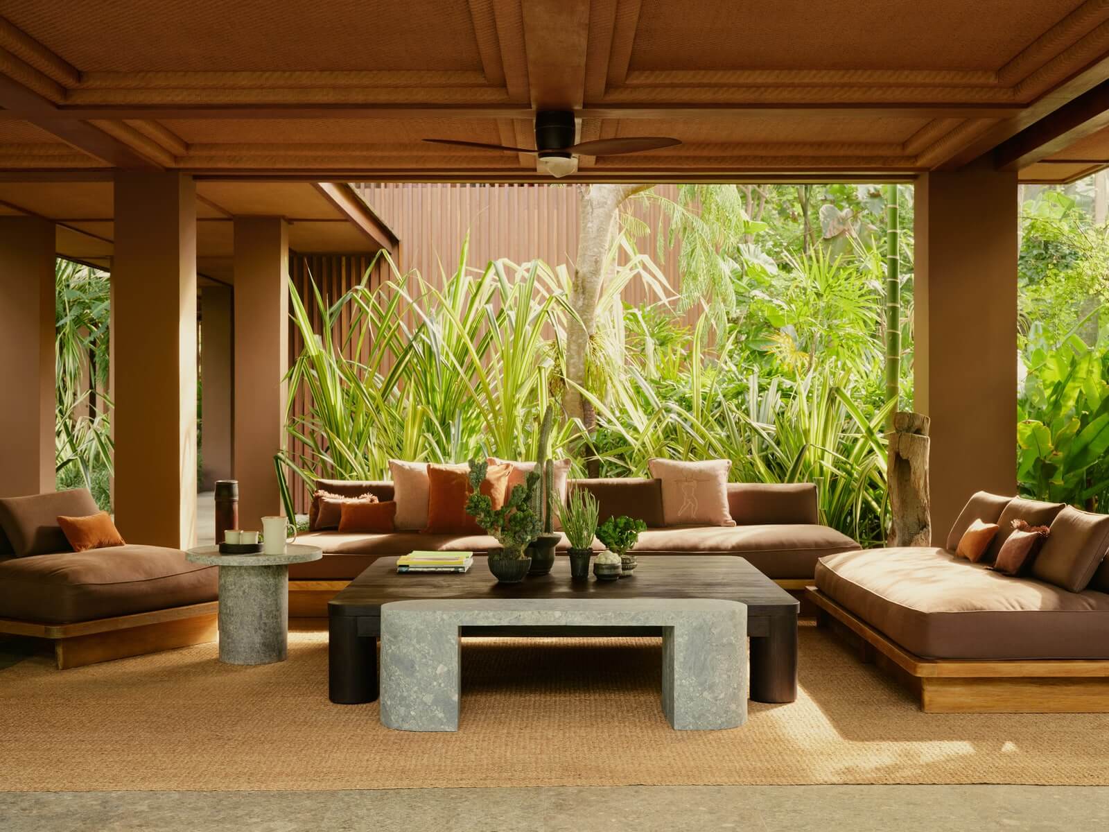 Lost Lindenberg, Asia — Covered pavilion with timber ceiling, earth-toned seating, concrete table, lush tropical plants, natural light filtering through open sides.
