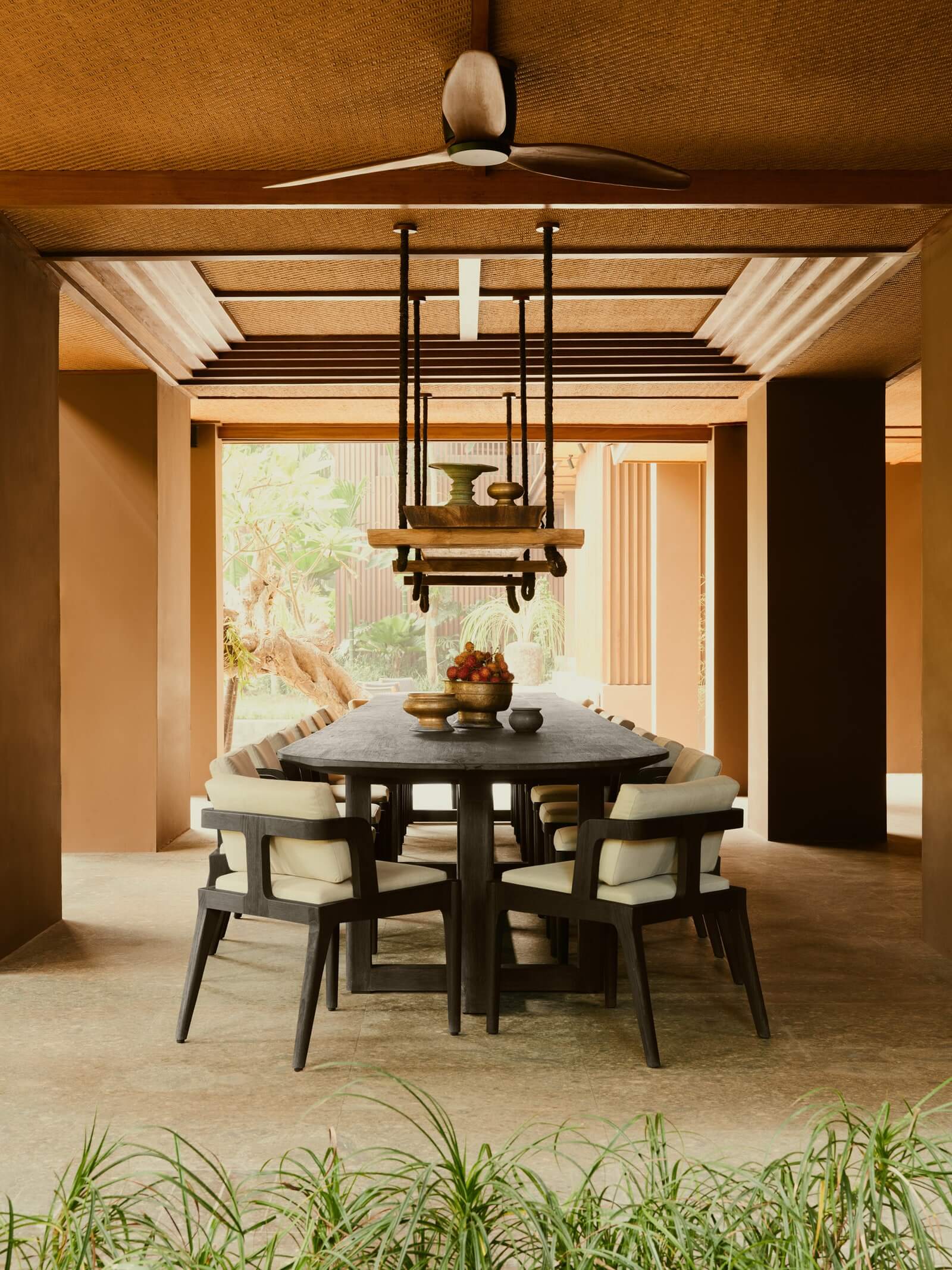 Lost Lindenberg, Asia — Circular black dining table with cream chairs beneath sculptural wood pendant, warm terracotta walls, natural light, modernist interior design.