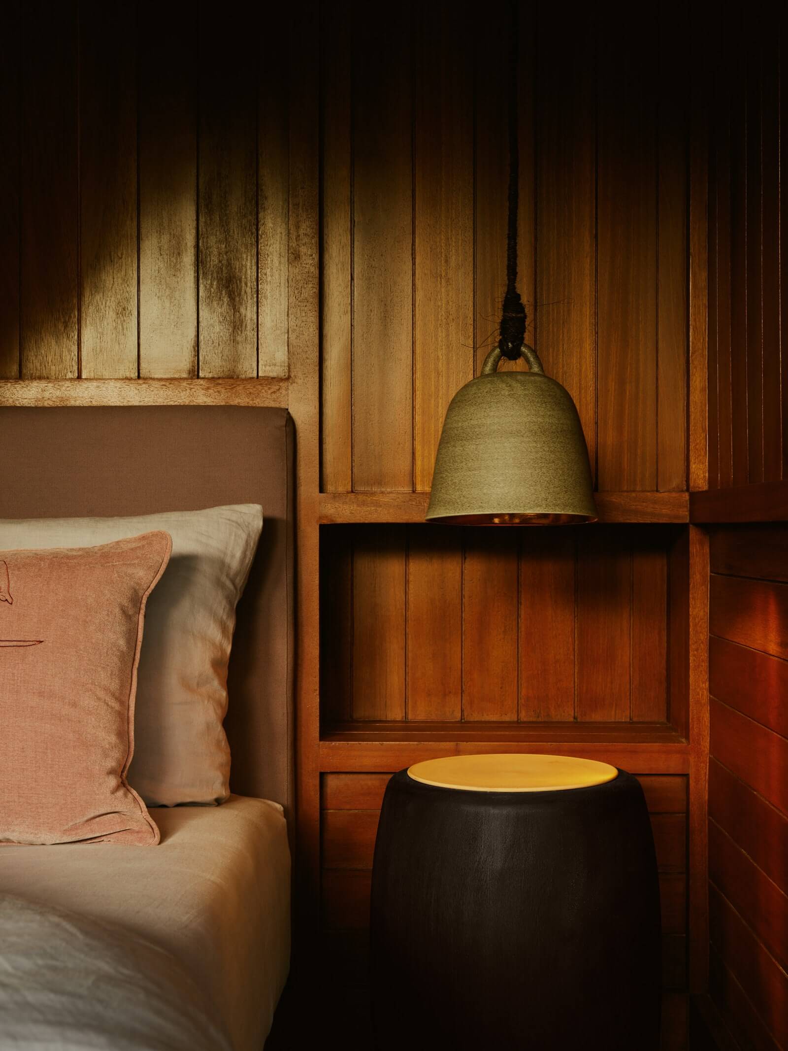 Lost Lindenberg, Asia — Wooden bedside table with brass pendant lamp, black ceramic side table, and warm-toned wood paneling in minimalist luxury bedroom.