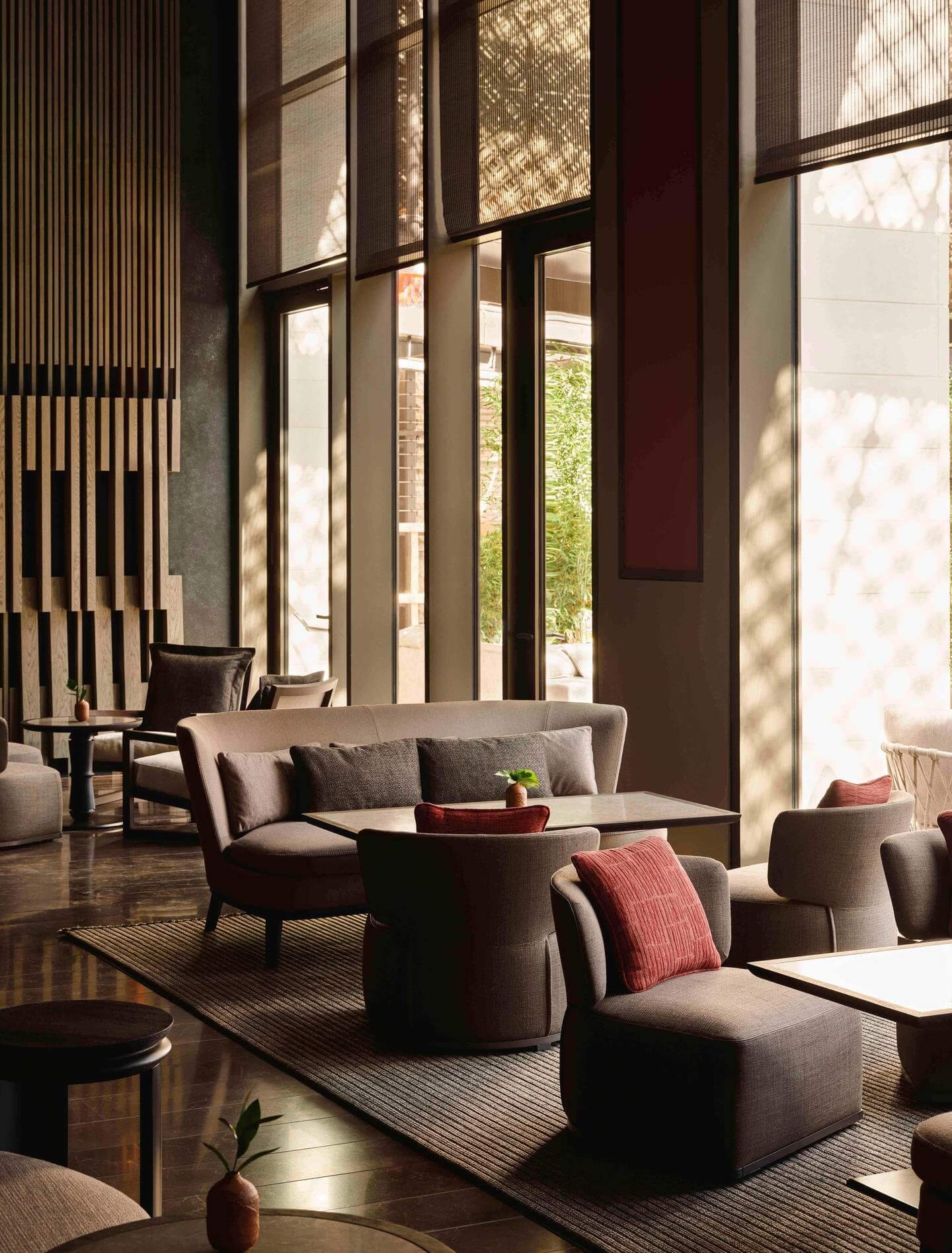Aman New York, North America — Modern luxury lounge with curved taupe seating, dark wood accents, floor-to-ceiling windows, natural light, and minimalist architectural details.