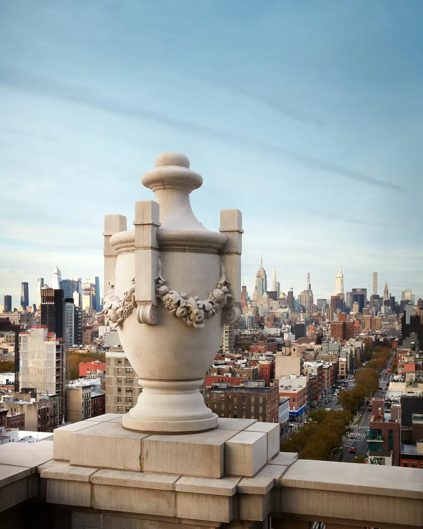 Nine Orchard, New York, United States — Neoclassical stone urn with garland detail on rooftop terrace overlooking Manhattan skyline and urban architecture.