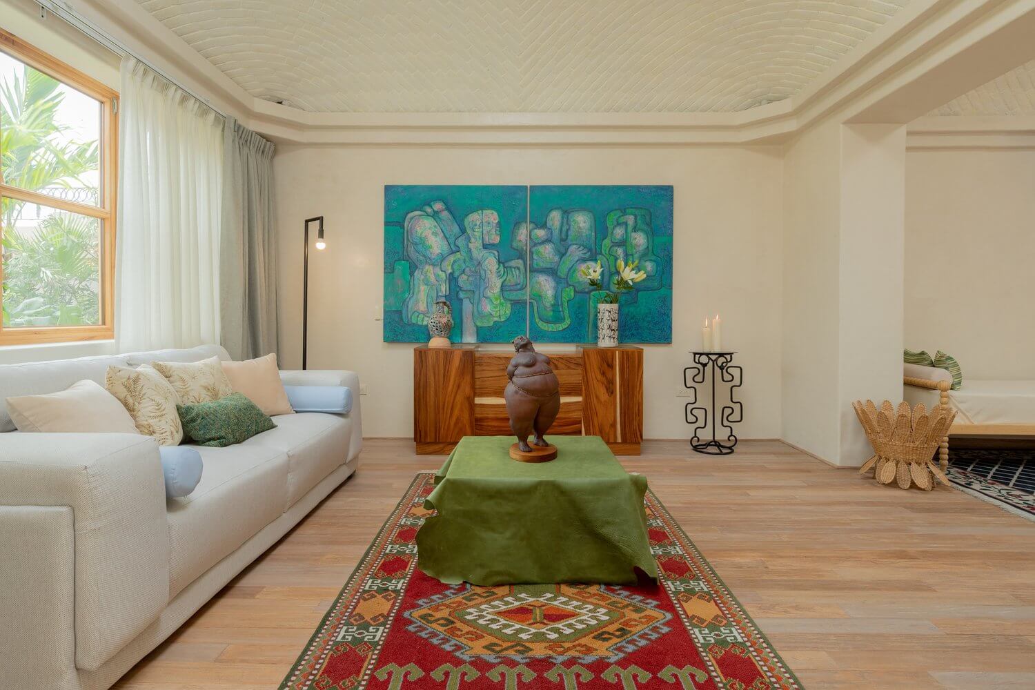 La Valise San Miguel, Mexico — Minimalist living room with cream sofa, turquoise abstract artwork, wooden dresser, and woven accents on warm wood flooring.