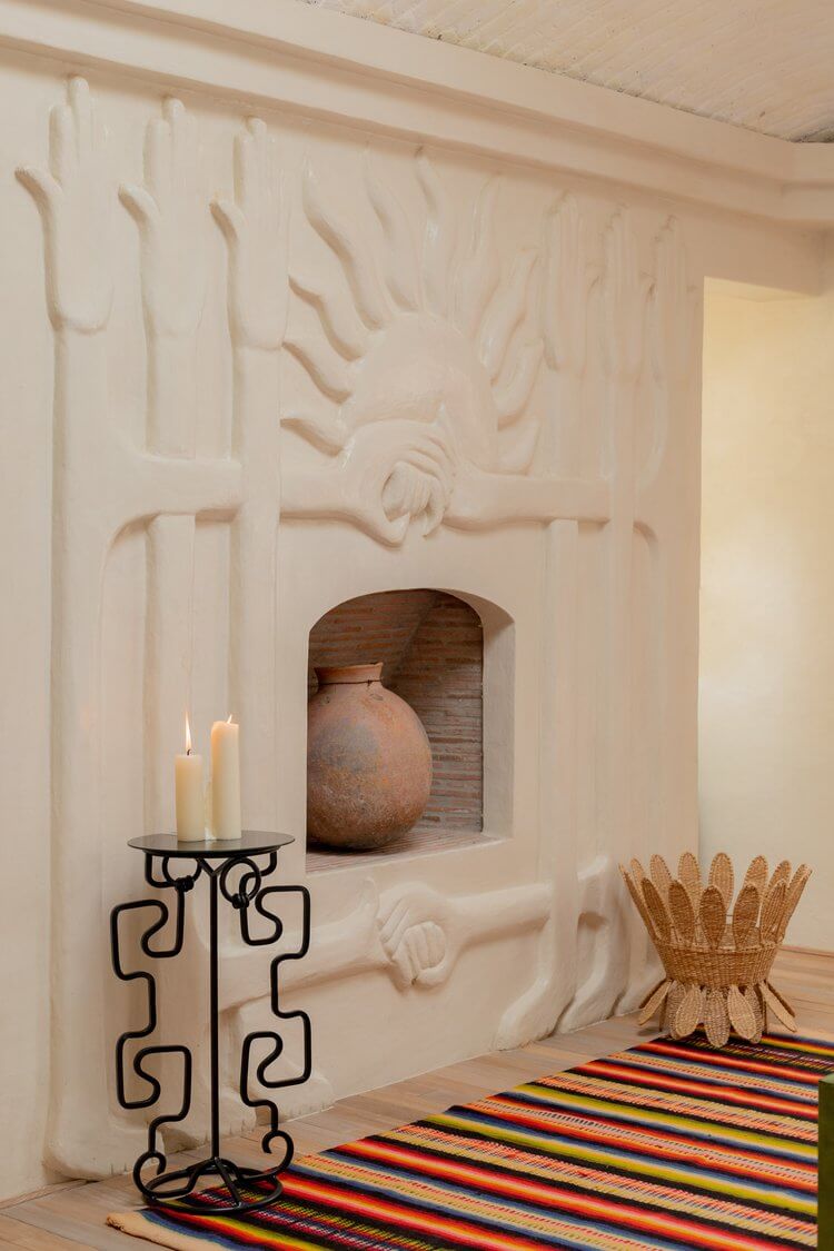 La Valise San Miguel, Mexico — Sculptural plaster wall with embedded niche displaying terracotta vessel, iron candelabra with candles, and striped textile floor detail.