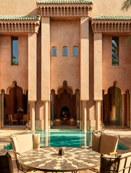 Amanjena, Morocco — Terracotta riad with arched doorways, geometric tilework, and turquoise pool reflecting minimalist luxury architecture and desert light.