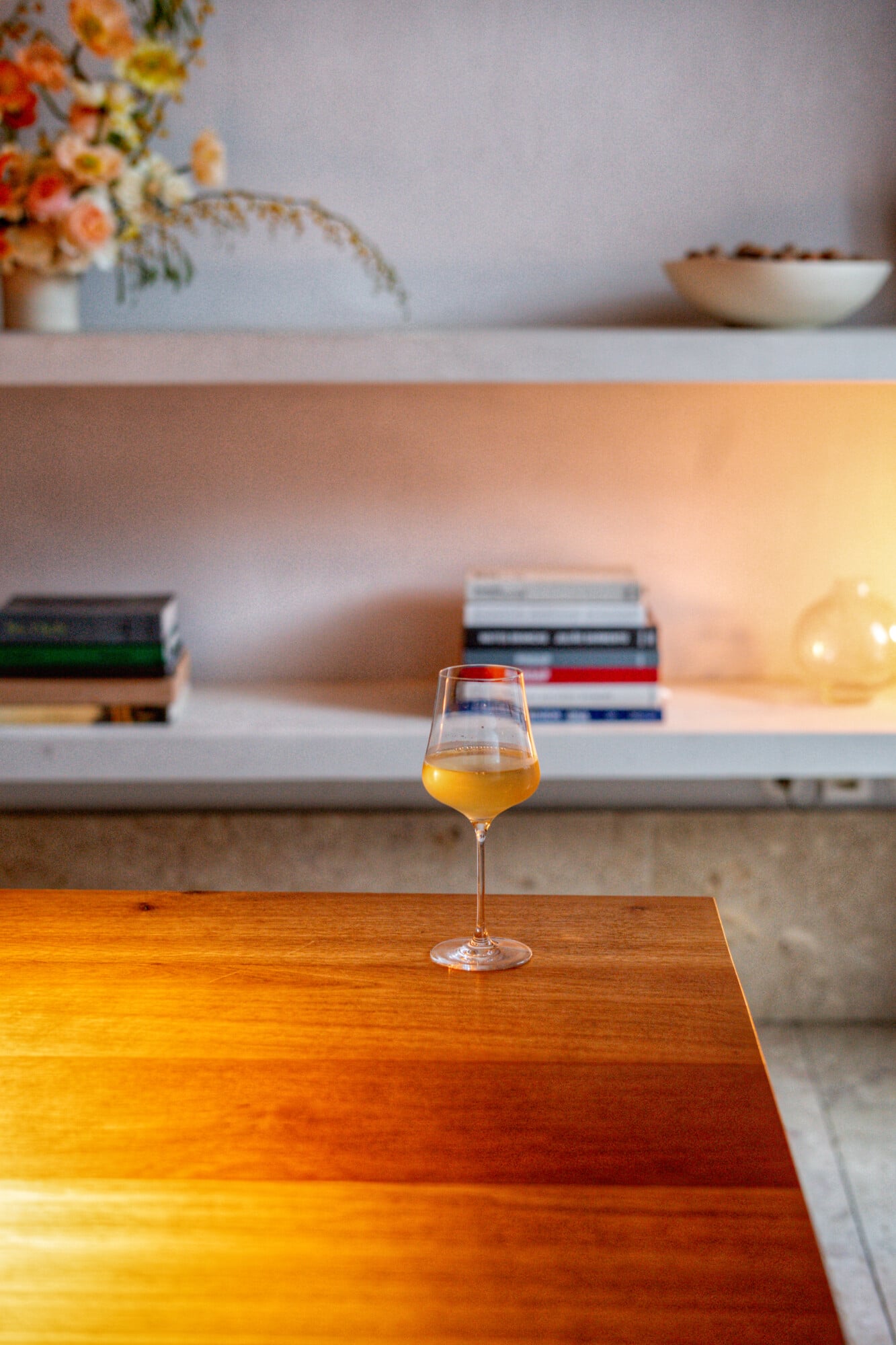 Santa Clara 1728, Portugal — Golden wine glass on warm wood table with blurred shelving, flowers, and soft natural light in luxury interior.
