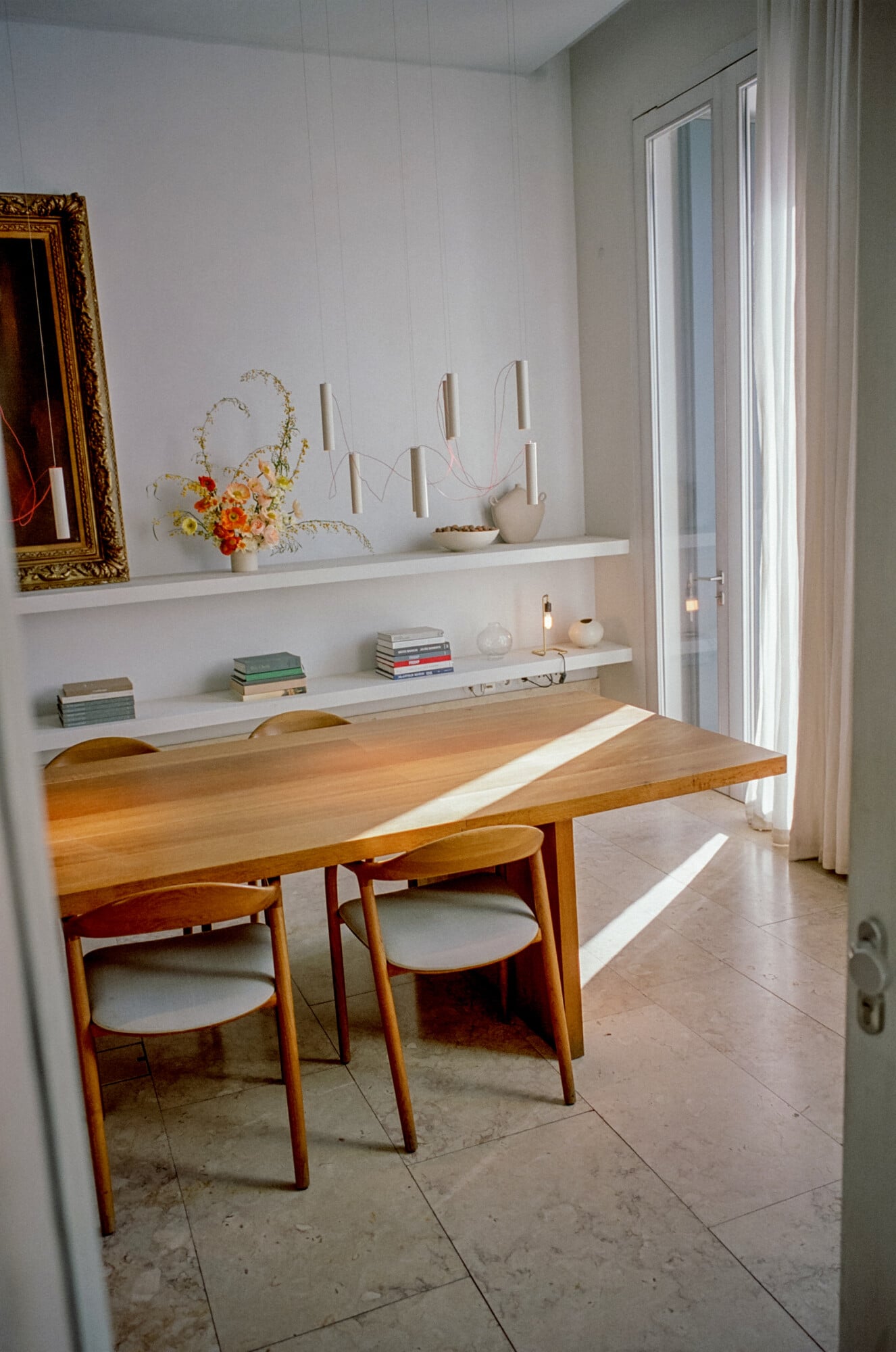 Santa Clara 1728, Portugal — Minimalist dining room with warm wood table, mid-century chairs, floating white shelves, natural light, and contemporary ceramic vessels.