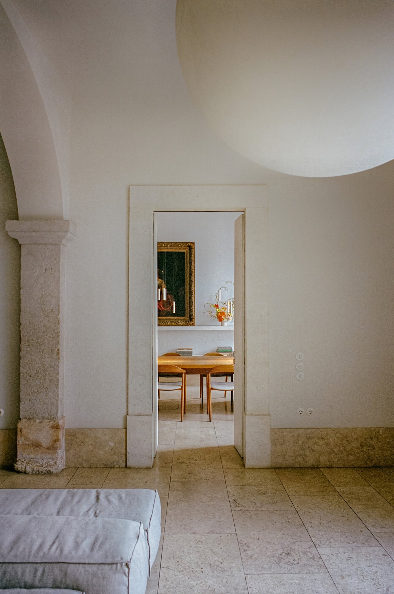 Santa Clara 1728, Portugal — Minimalist corridor with stone columns, curved ceiling, natural light, wooden dining table visible through open doorway.