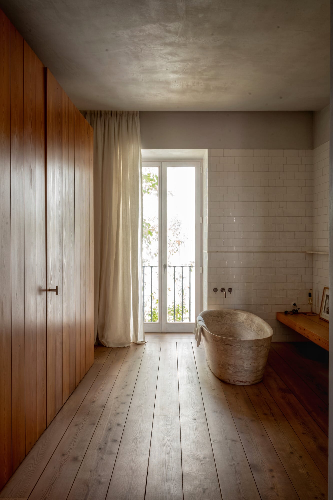 Santa Clara 1728, Portugal — Spa bathroom with stone soaking tub, wooden cabinetry, subway tile walls, light-filled French doors opening to terrace, natural materials and minimalist design.