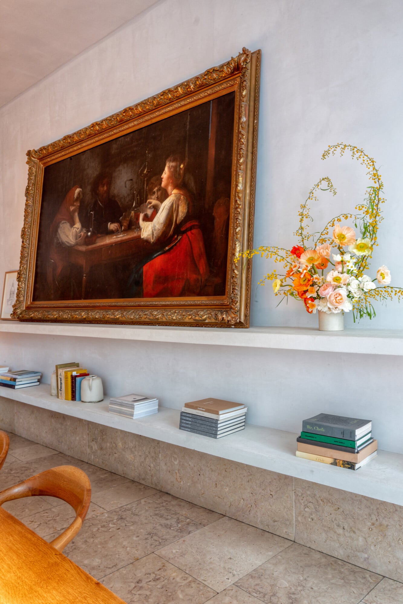 Santa Clara 1728, Portugal — Minimalist gallery wall with gilt-framed Old Master painting, fresh floral arrangement, stacked books, and travertine shelving in luxury hotel interior.