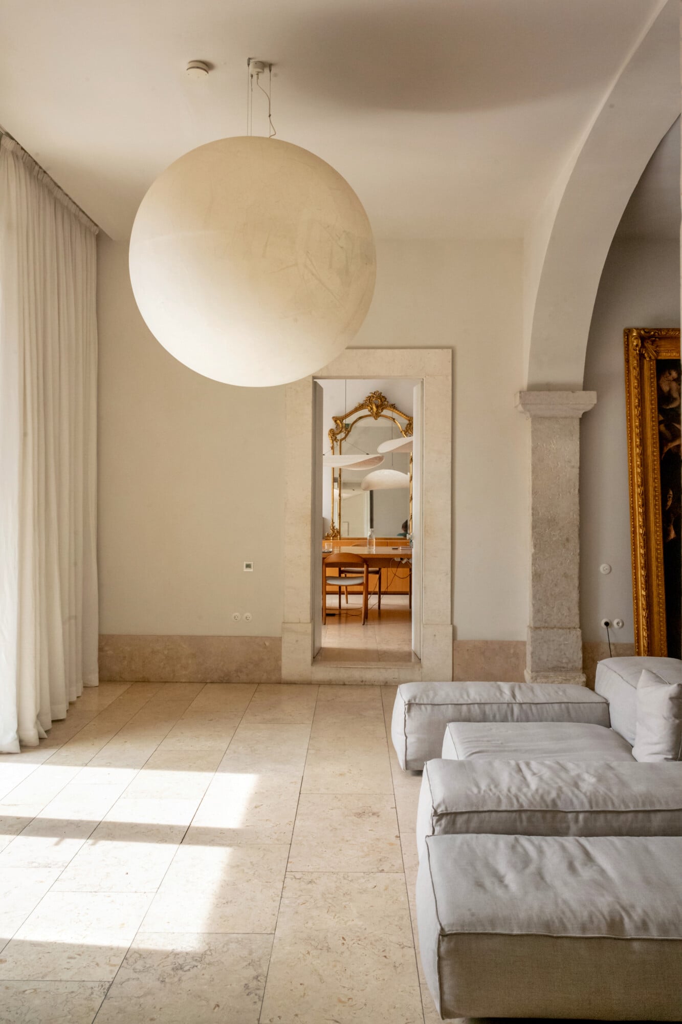 Santa Clara 1728, Portugal — Minimalist bedroom with cream walls, large spherical pendant light, stone flooring, arched architectural details, and gilt-framed artwork.