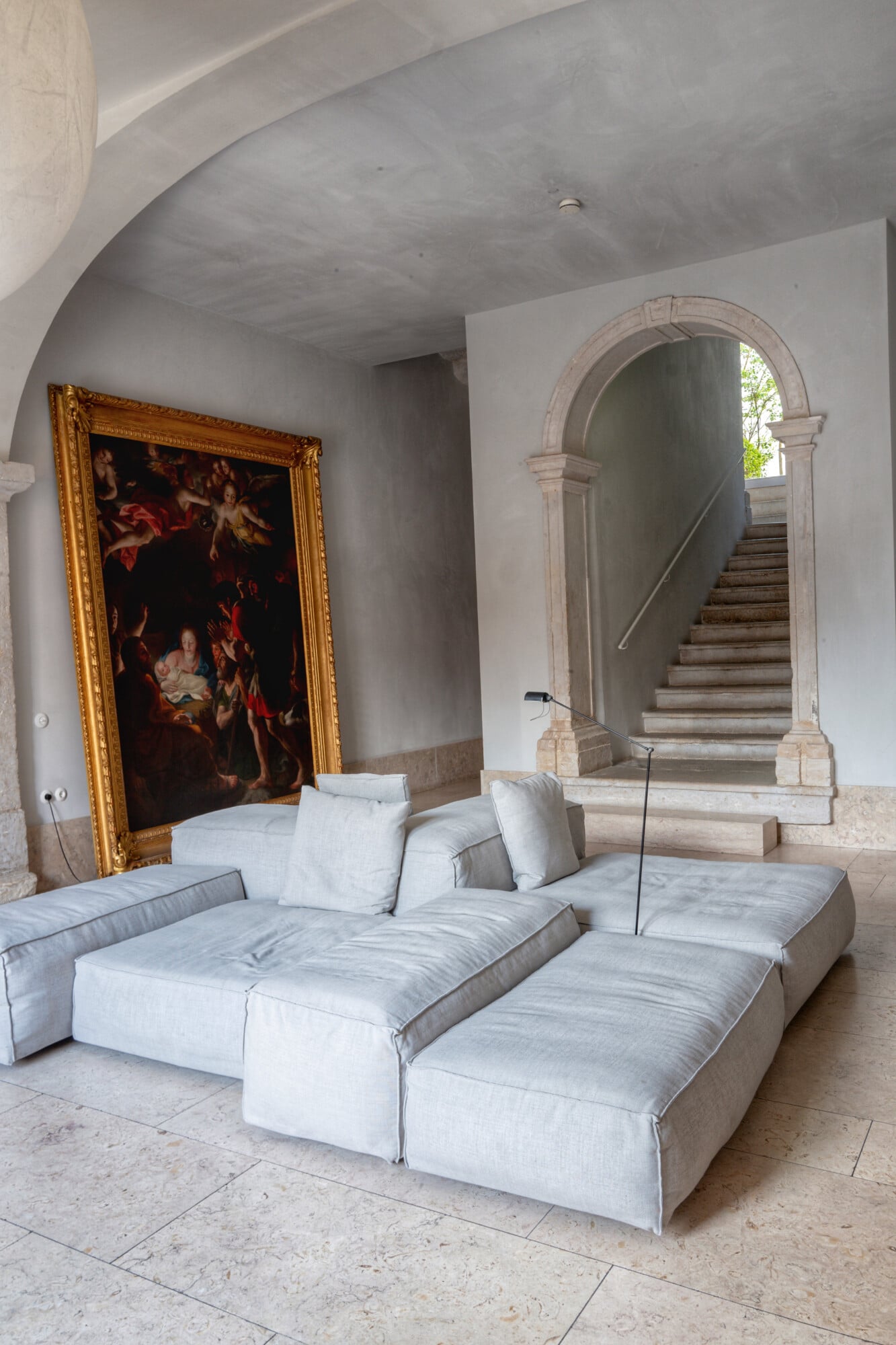 Santa Clara 1728, Portugal — Minimalist linen seating arrangement beneath arched stone doorway and baroque gilt-framed painting in austere whitewashed gallery space.