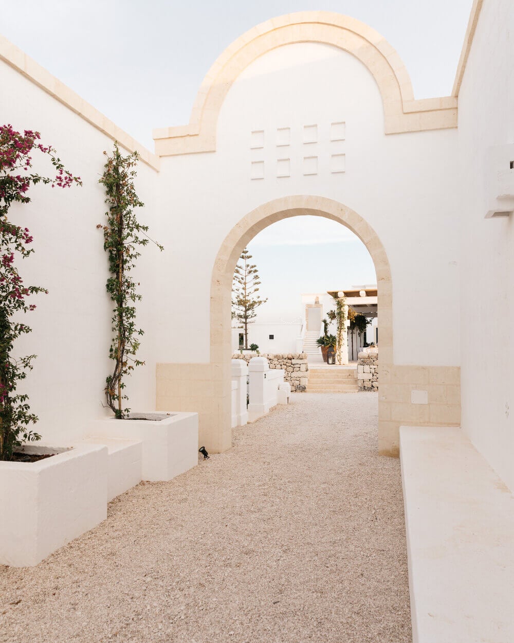 Masseria Calderisi, Europe — Arched stone passageway with whitewashed walls, terracotta ground, cascading magenta bougainvillea, and bright Mediterranean courtyard beyond.