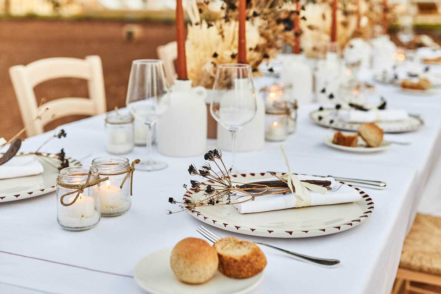 Masseria Calderisi, Europe — Long table set with white linens, dried florals, candles, and place settings overlooking terracotta landscape.