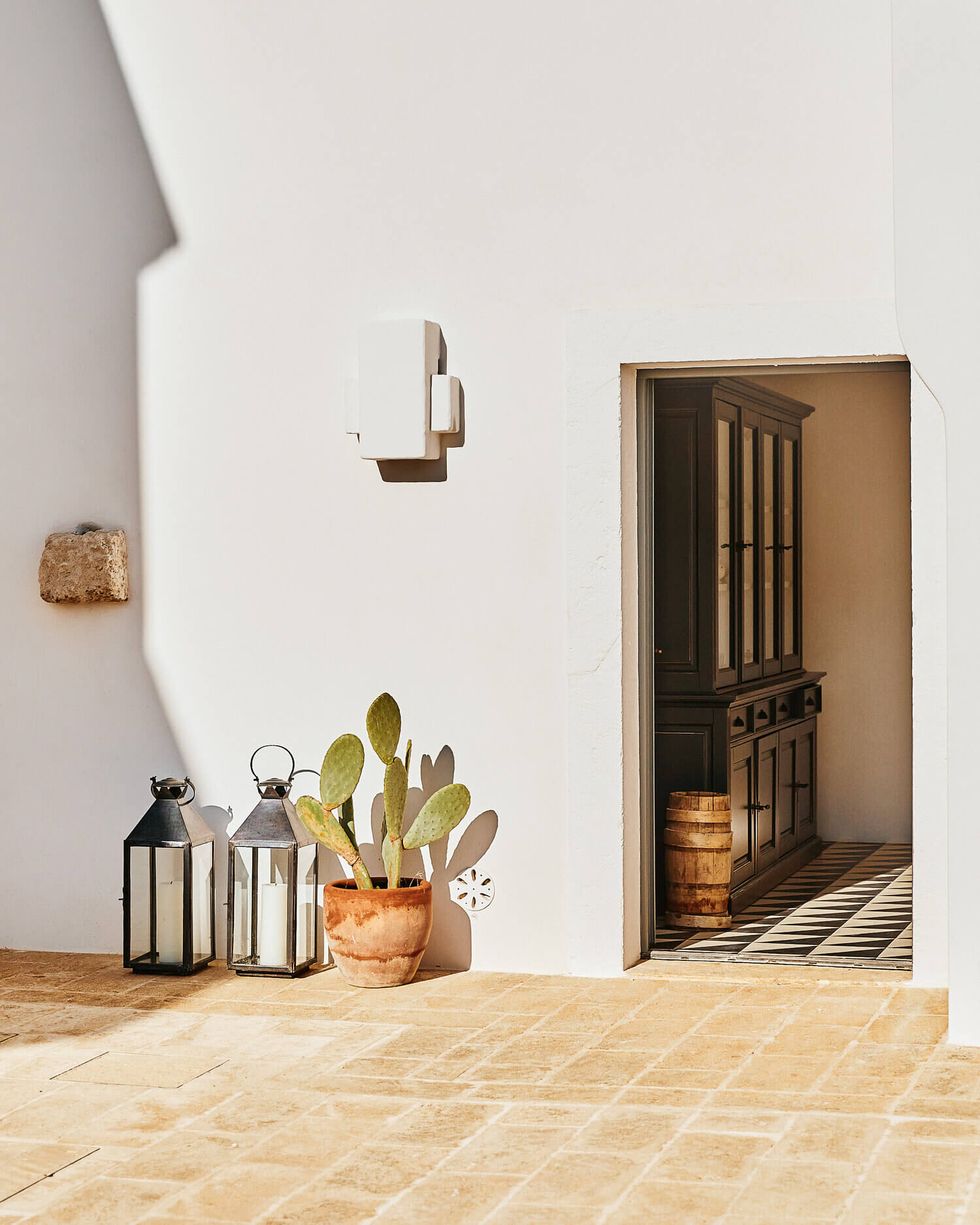 Masseria Calderisi, Europe — Whitewashed courtyard with terracotta pots, black lanterns, wooden doors, and geometric stone flooring in Mediterranean luxury design.