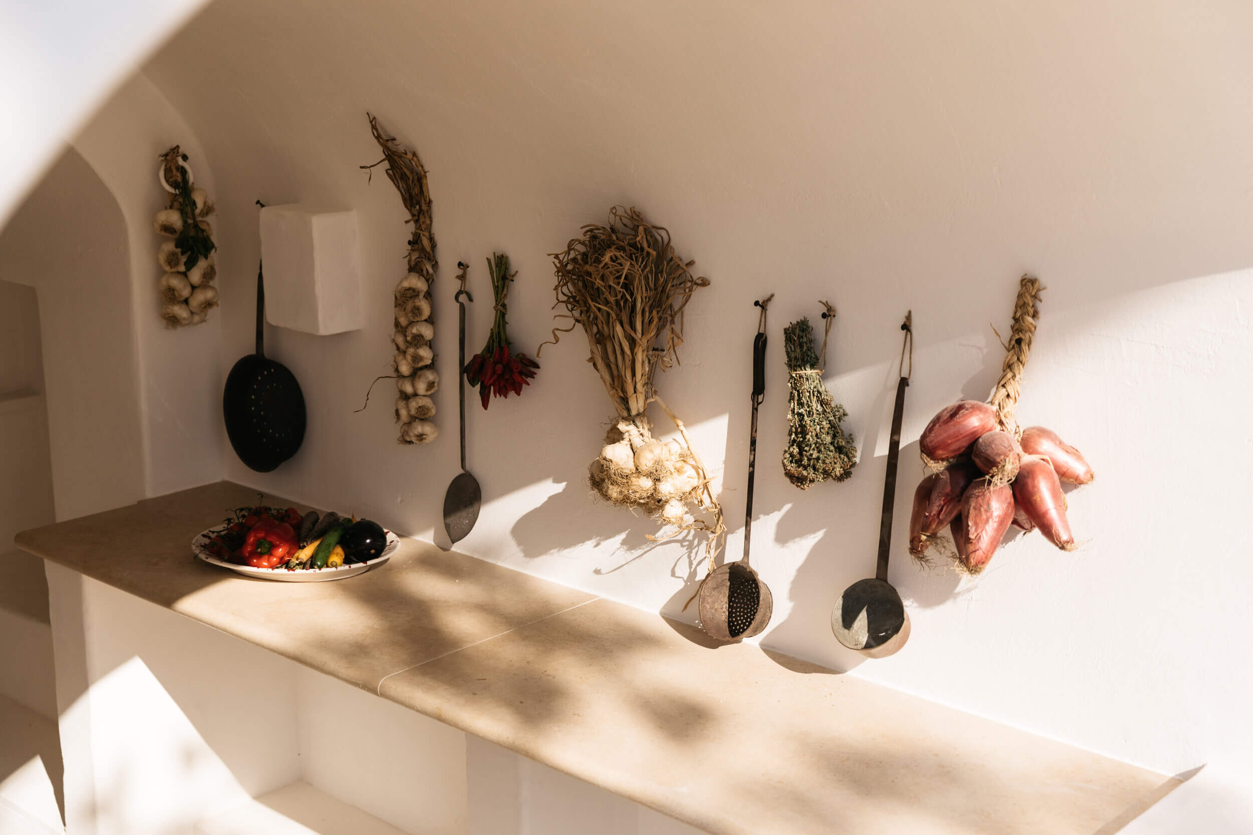 Masseria Calderisi, Europe — Dried botanicals and vintage kitchen utensils arranged on whitewashed wall in sunlit culinary display.
