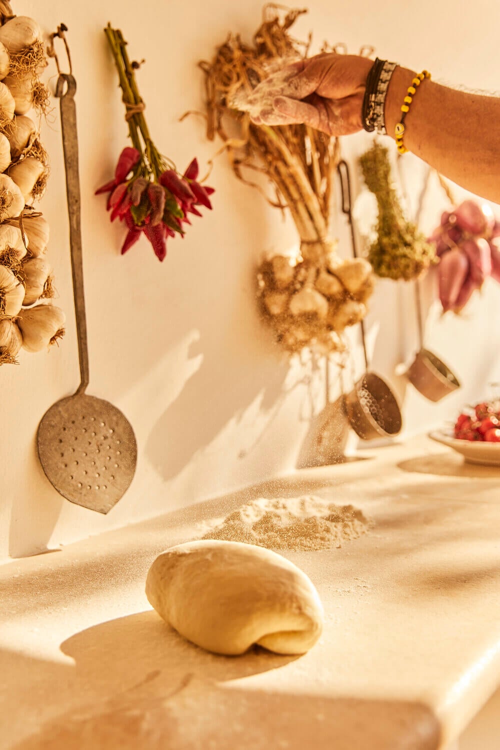 Masseria Calderisi, Europe — Dried herbs and garlic hanging above flour-dusted kitchen counter with artisanal cooking tools in warm natural light.