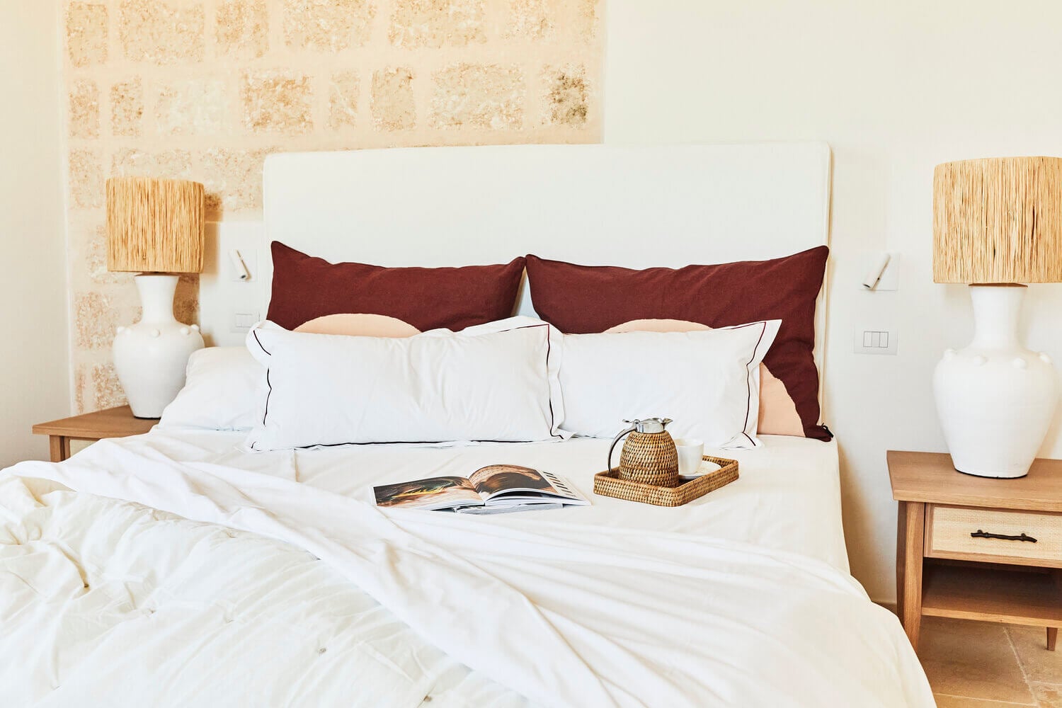Masseria Calderisi, Europe — Bedroom with white linens, burgundy pillows, wooden nightstands, woven accents, and terracotta brick wall detail.