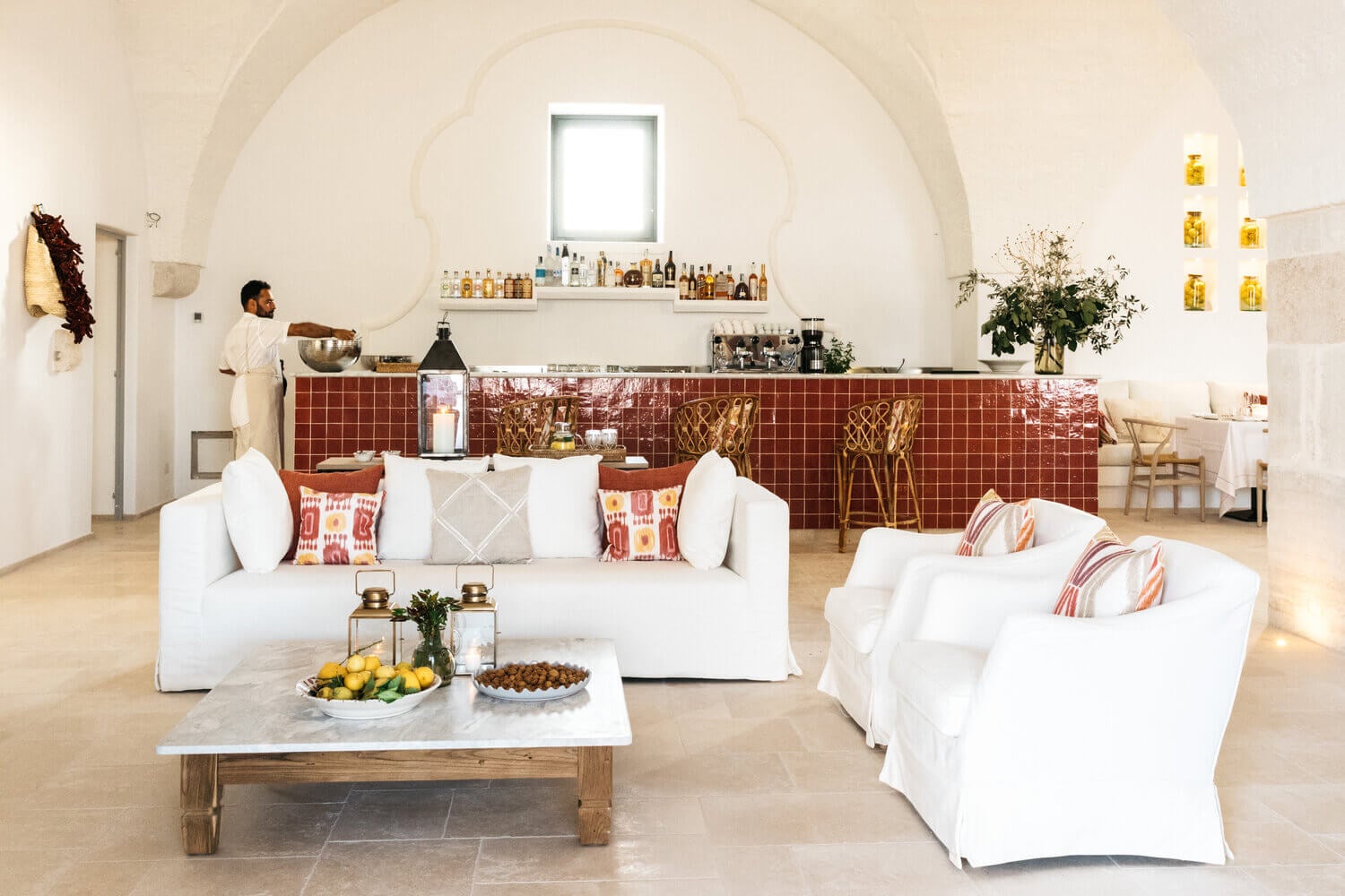 Masseria Calderisi, Europe — Arched whitewashed lounge with terracotta tile bar, linen seating, marble coffee table, and natural light from clerestory window.