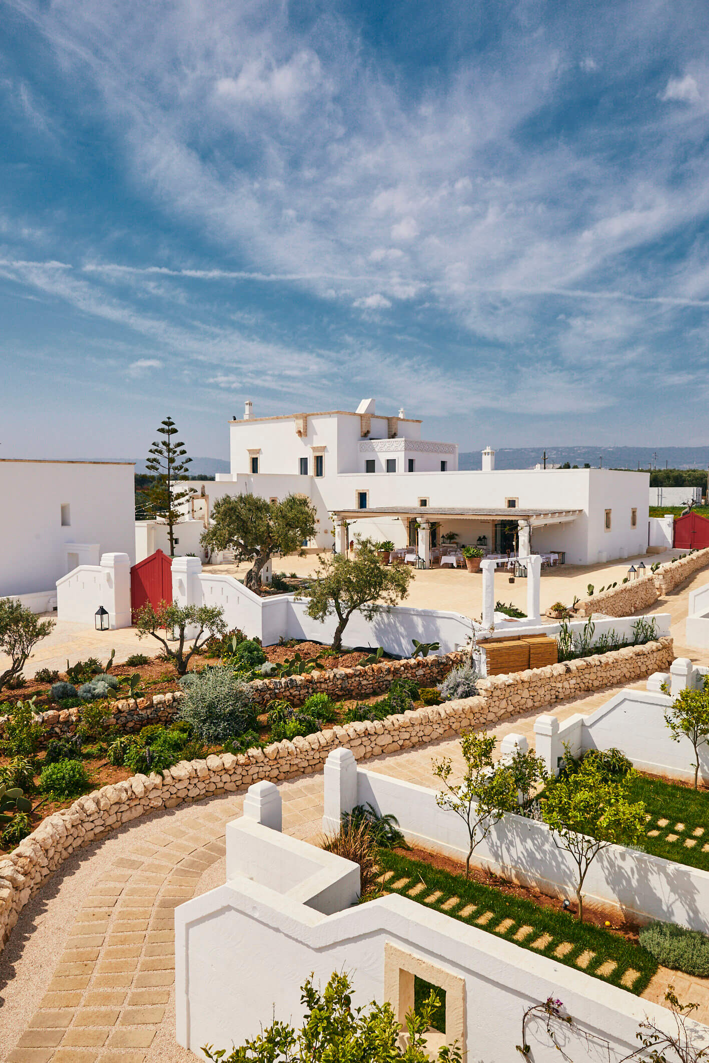 Masseria Calderisi, Europe — Whitewashed Mediterranean villa with columned portico, terraced gardens, stone walls, and olive trees under blue sky.