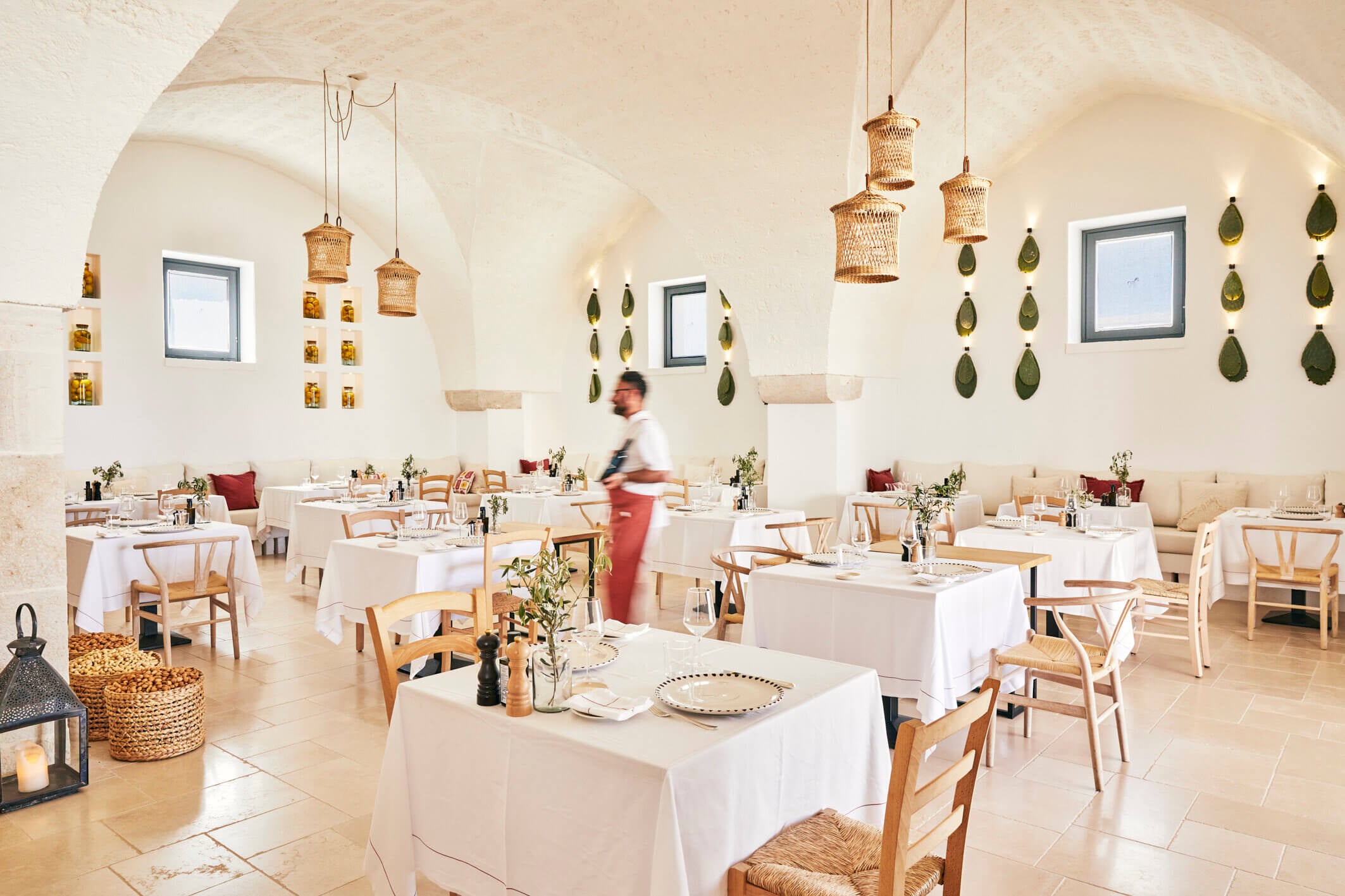 Masseria Calderisi, Europe — Vaulted dining room with woven pendant lights, natural stone floors, wooden chairs, and hanging olive-shaped ceramic vessels.