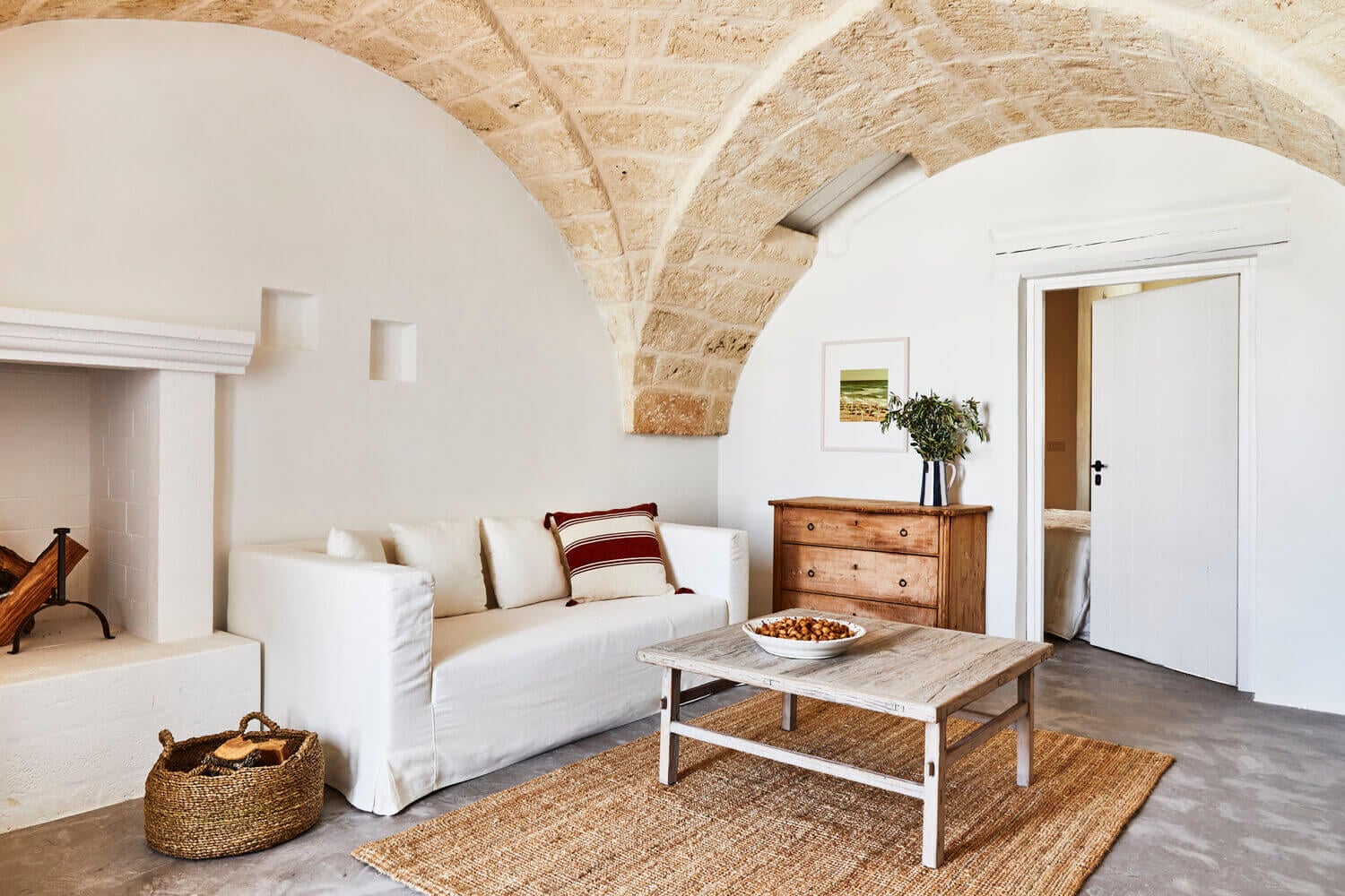 Masseria Calderisi, Europe — Arched stone ceiling, white-slipcover sofa, weathered wood table, natural light in minimalist Mediterranean room.