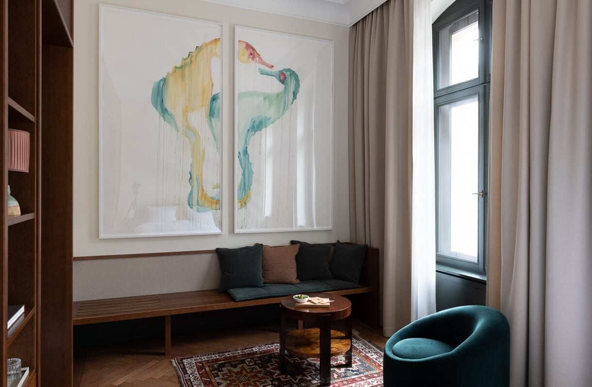 Château Royal, Europe — Contemporary lounge with watercolor seahorse artwork, wooden bench seating, teal accent chair, and floor-to-ceiling windows overlooking grounds.