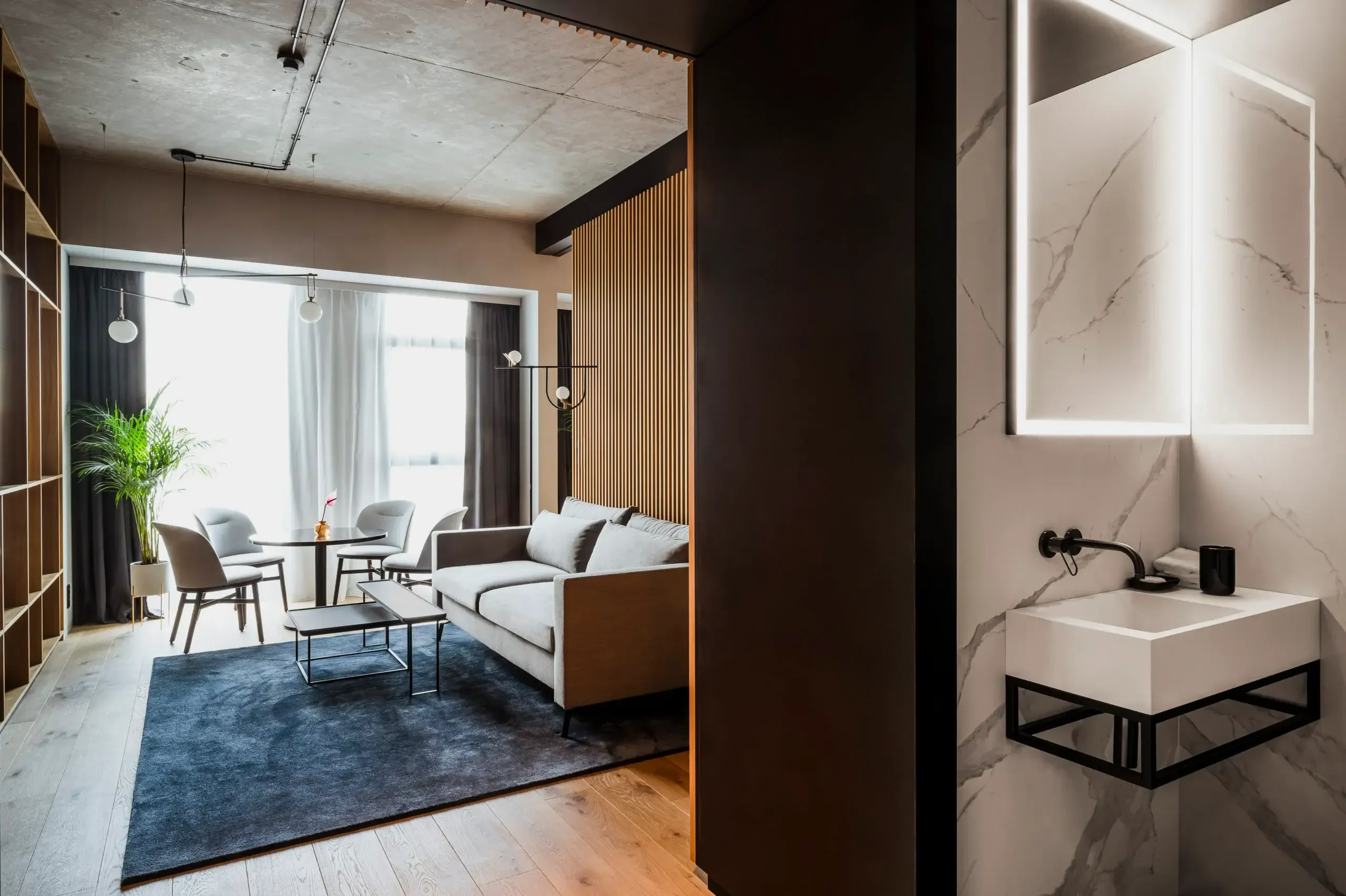 Nobu Warsaw, Poland — Modern hotel suite with marble bathroom, wood-slat accent wall, floor-to-ceiling windows, contemporary furniture, and ambient lighting.