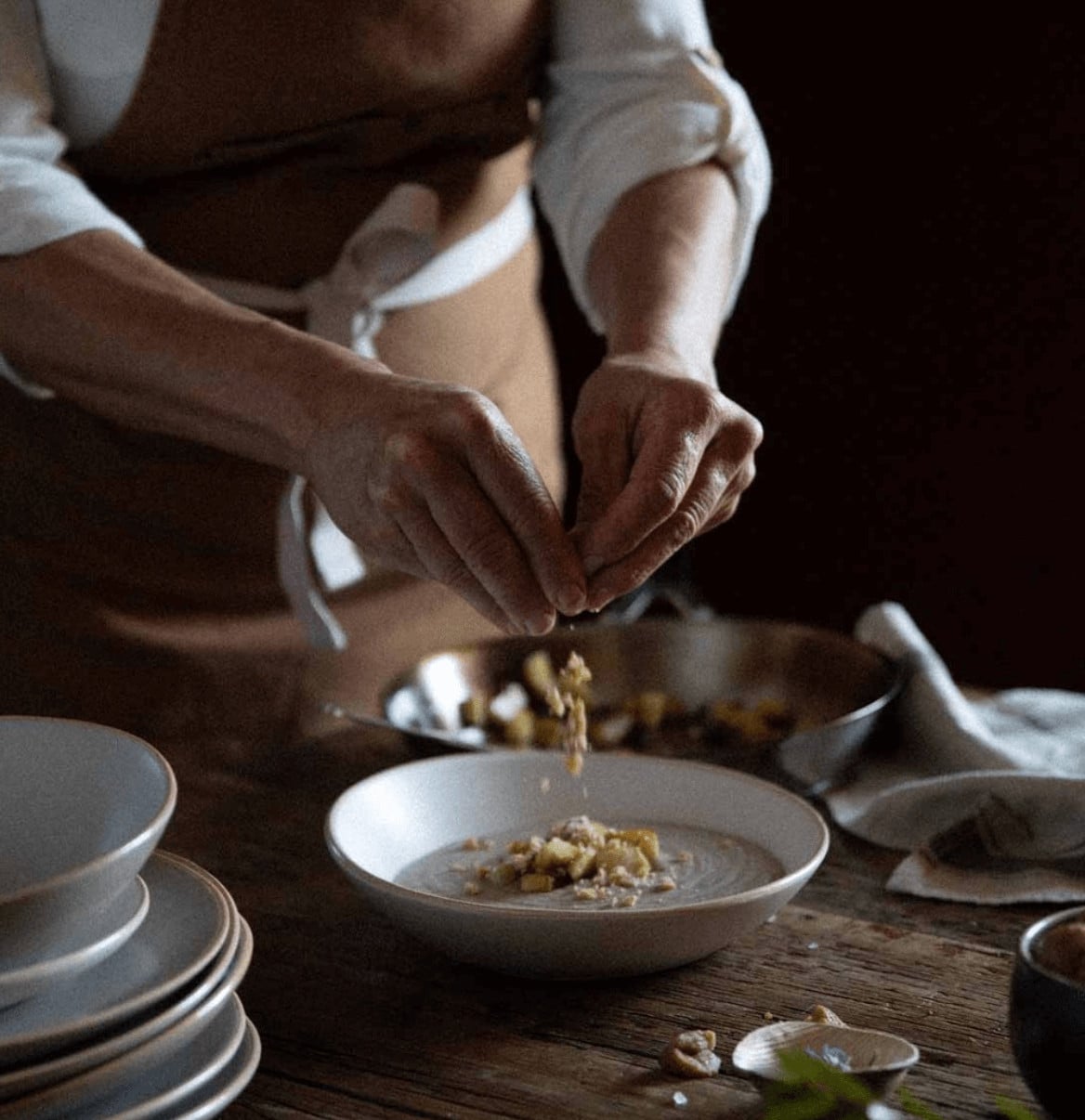 Culinary Academy — Chef plating delicate seafood dish with precise hands over white ceramic bowl, warm natural light, rustic wooden table setting, fine dining culinary experience.