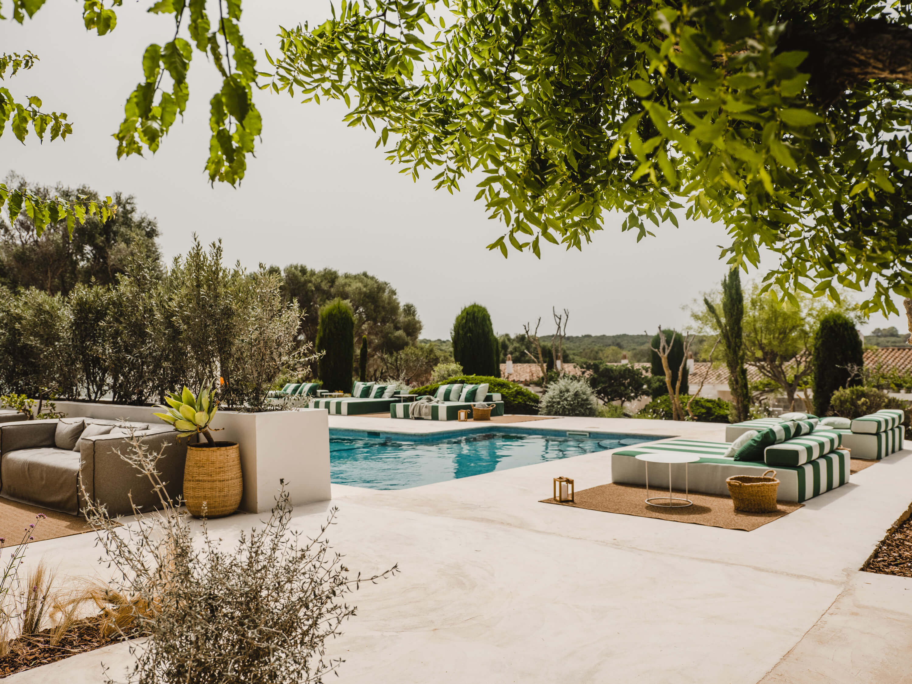 Morvedra Nou, Balearic Islands — modernist poolside terrace with striped loungers, limestone paving, cypress trees, and Mediterranean landscape under natural light.