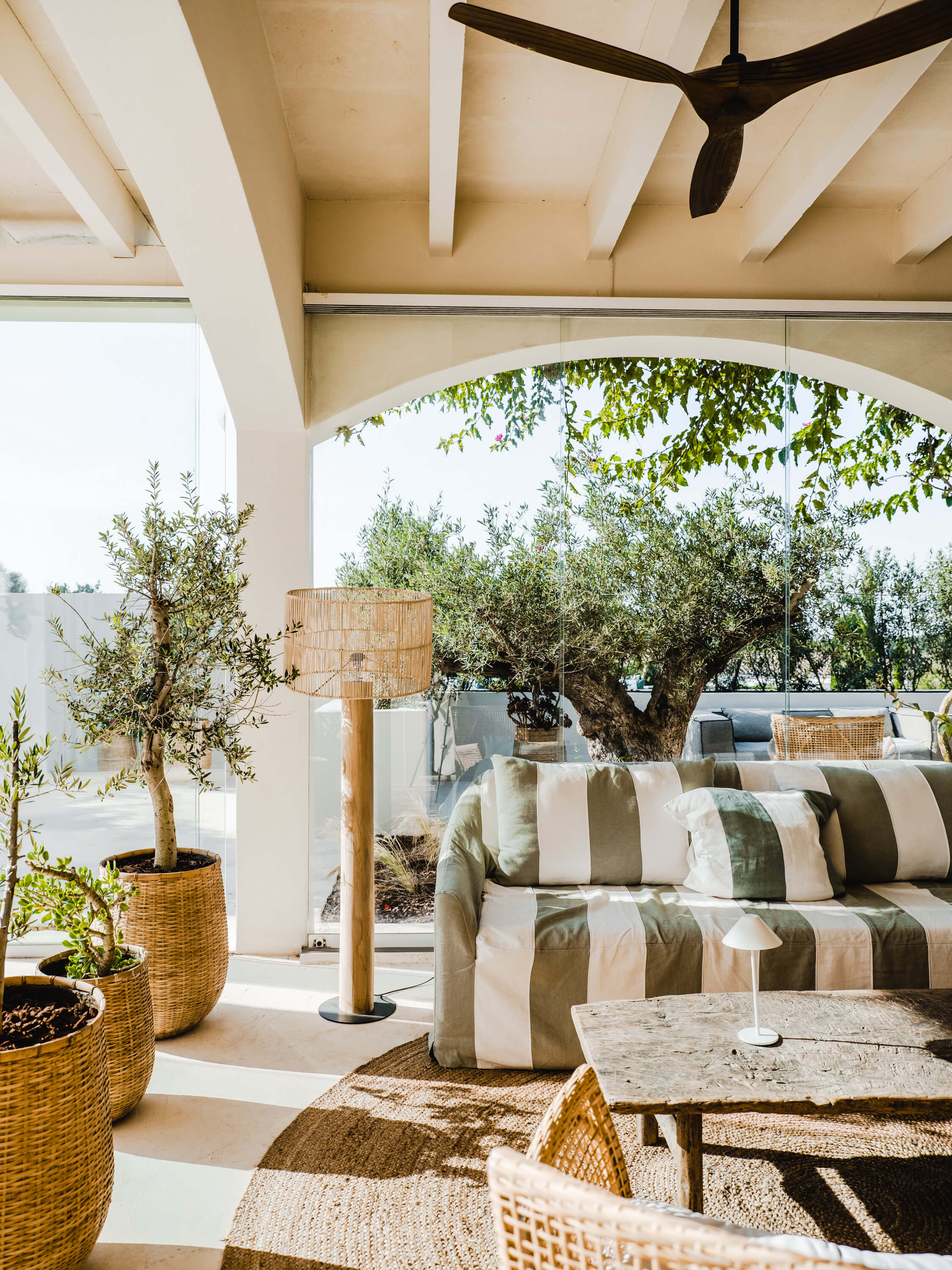 Morvedra Nou, Balearic Islands — Covered terrace with striped seating, arched ceiling, potted olive trees, and view to Mediterranean landscape.