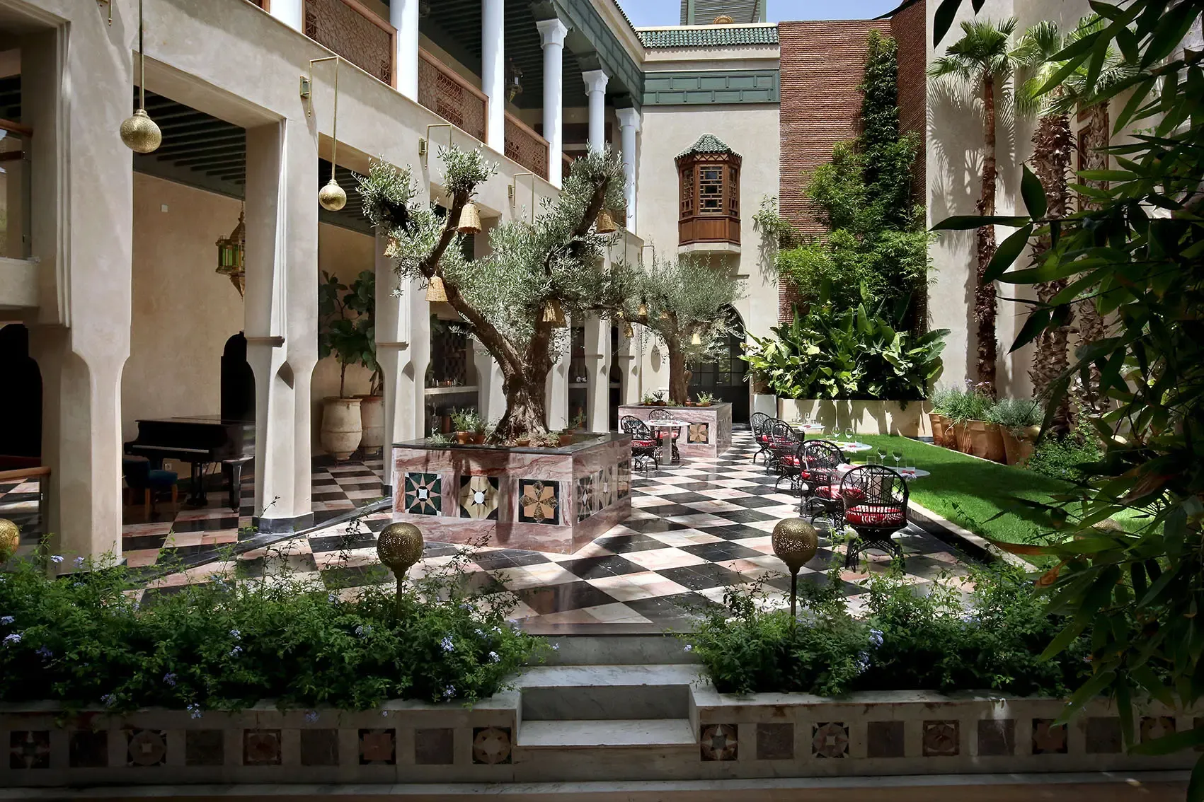 Colonnade Bar, Africa — Moroccan riad courtyard with black-and-white tile floors, white columns, olive trees, brass hanging lamps, and arched doorways opening to guest rooms.