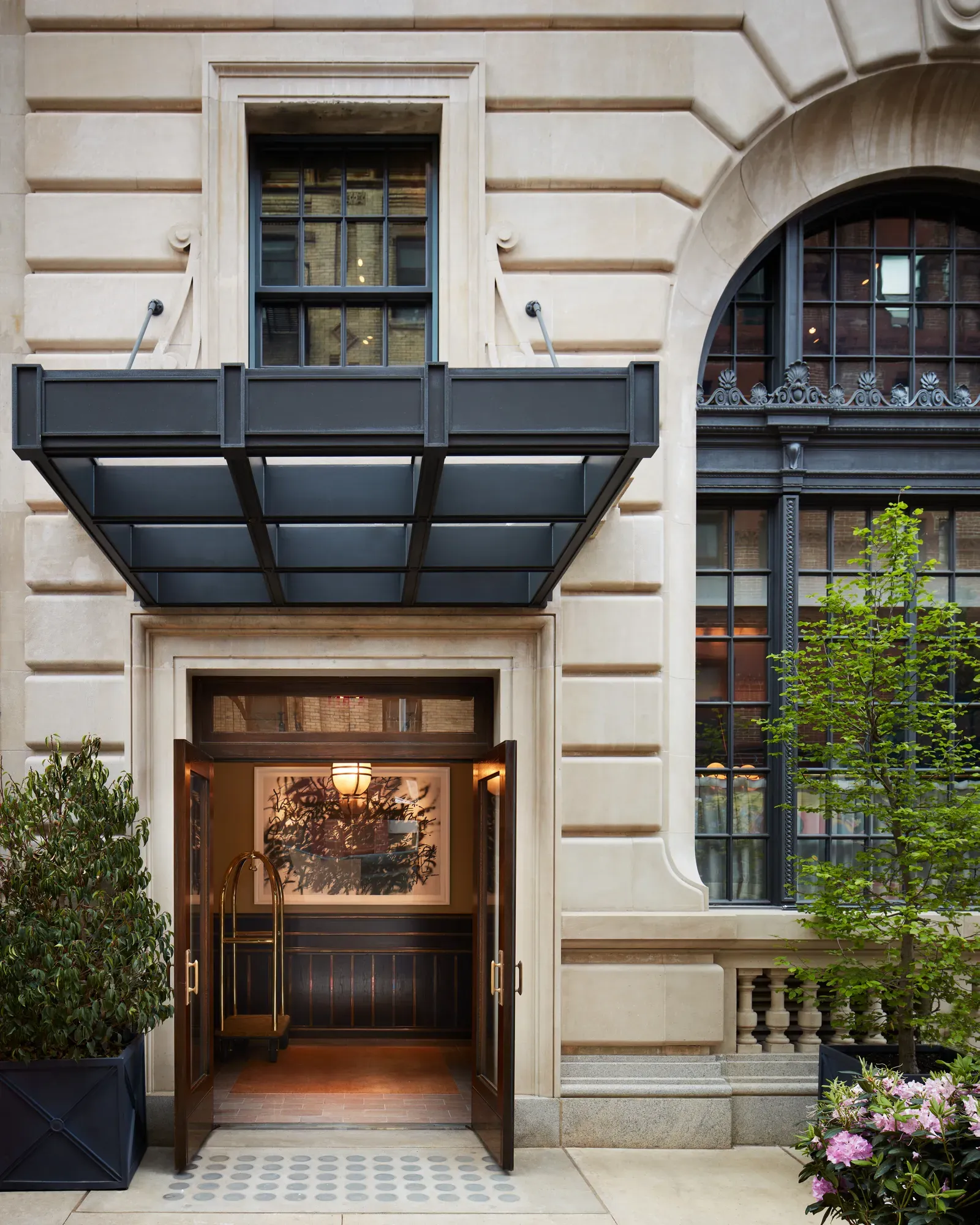 Nine Orchard, New York, USA — Cream limestone façade with black steel canopy over bronze entry doors, arched window detail, modern luxury townhouse architecture.