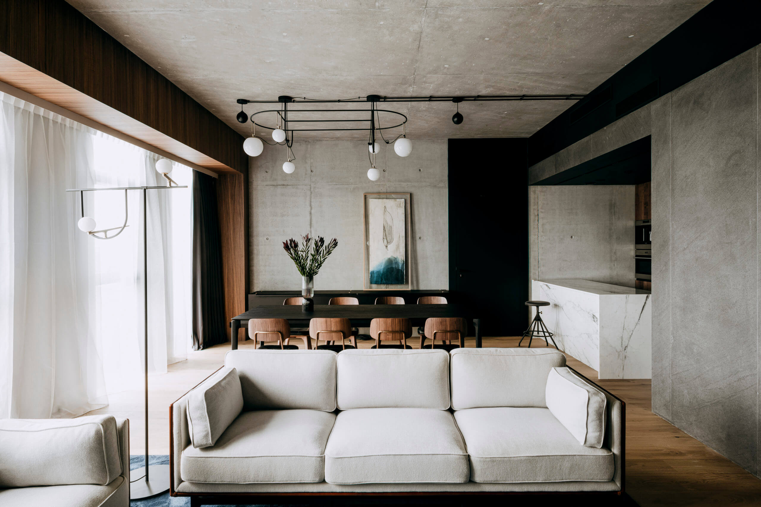 Nobu Warsaw, Poland — Modern living room with cream sofa, concrete ceiling, wooden dining table, pendant lights, and minimalist aesthetic.