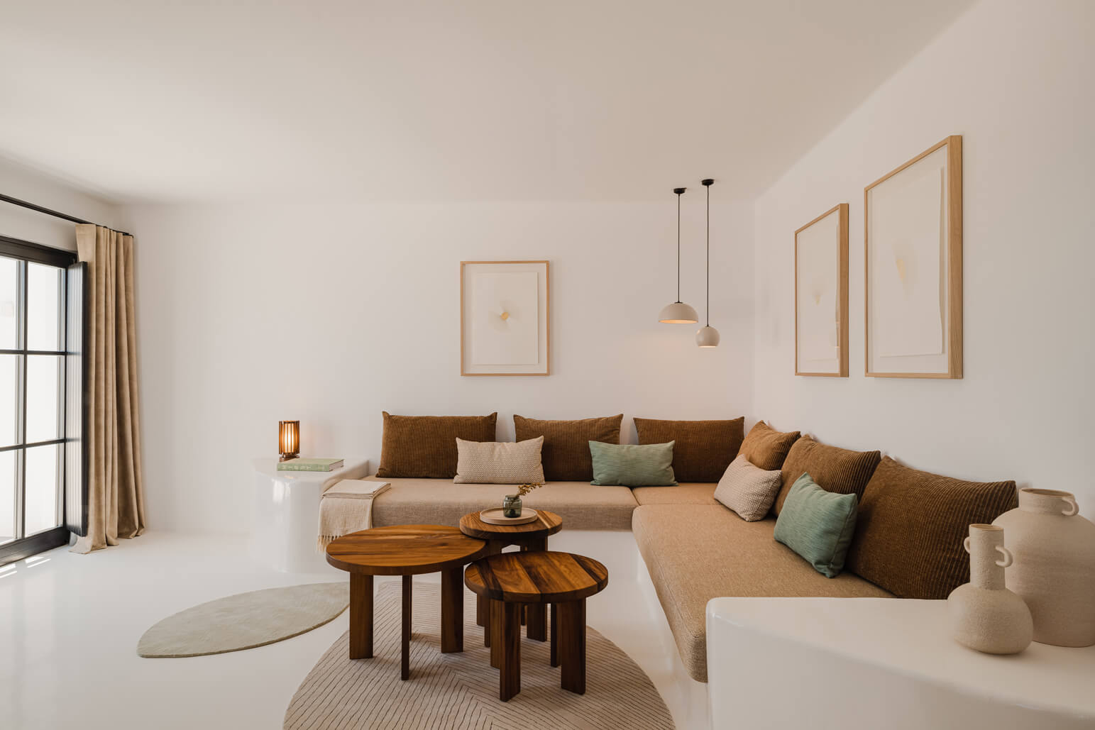 Nobu Santorini, Greece — Minimalist living room with natural linen sectional, warm wood side tables, terracotta pendant lights, and framed artwork against whitewashed walls.