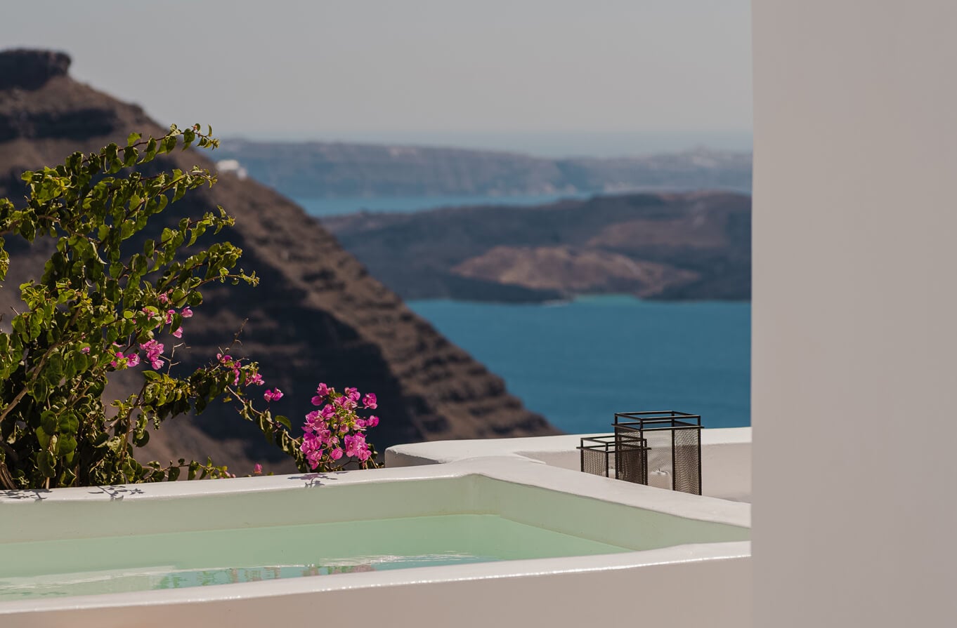 Nobu Santorini, Greece — infinity pool with turquoise water overlooking volcanic caldera, pink bougainvillea, white architecture and Aegean Sea vista.