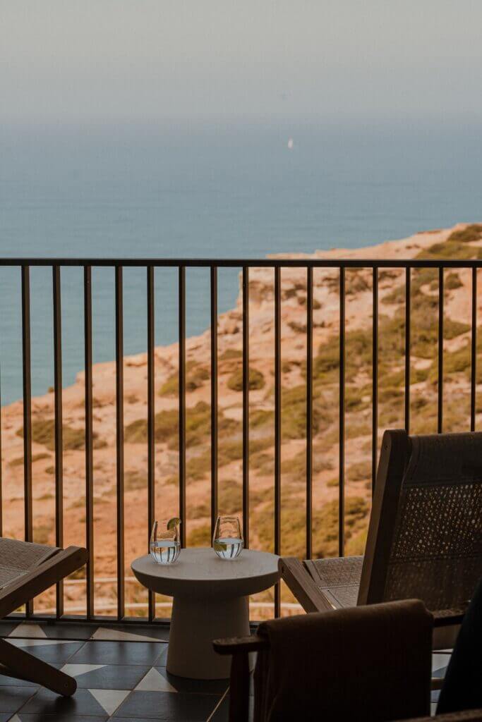 Aethos Ericeira, Portugal — Coastal balcony with black metal railing, minimalist furniture, and view of sandy cliffs overlooking calm sea.