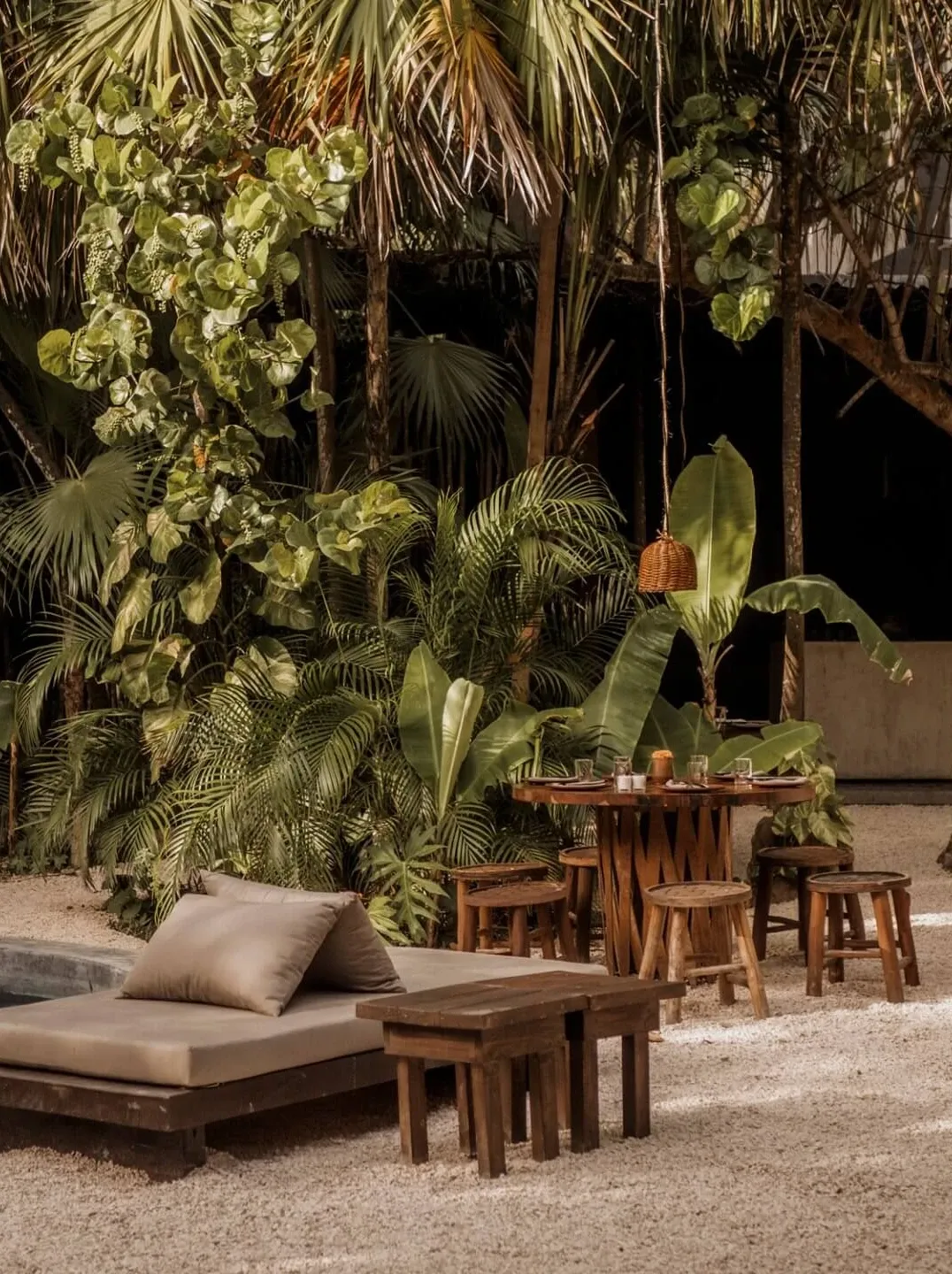 Tulum Treehouse, Mexico — Tropical night garden with wooden loungers, woven pendant lights, and layered palm fronds creating an intimate outdoor sanctuary.