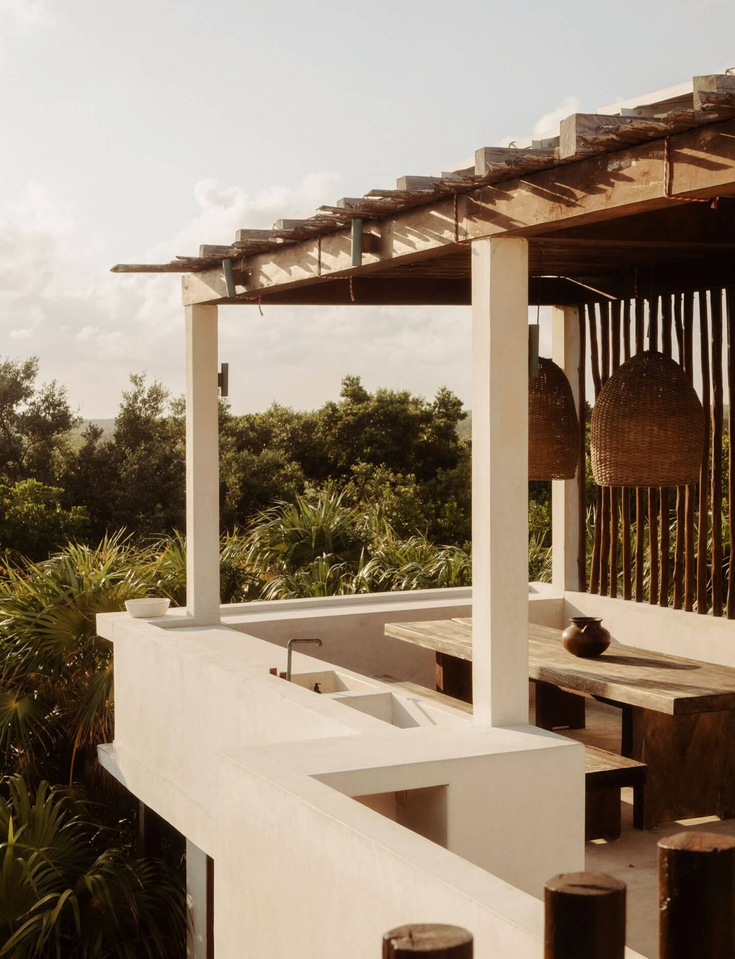 Tulum Treehouse, Mexico — Modernist terrace with white concrete pergola, woven hanging chairs, wooden benches, and panoramic jungle vista at golden hour.