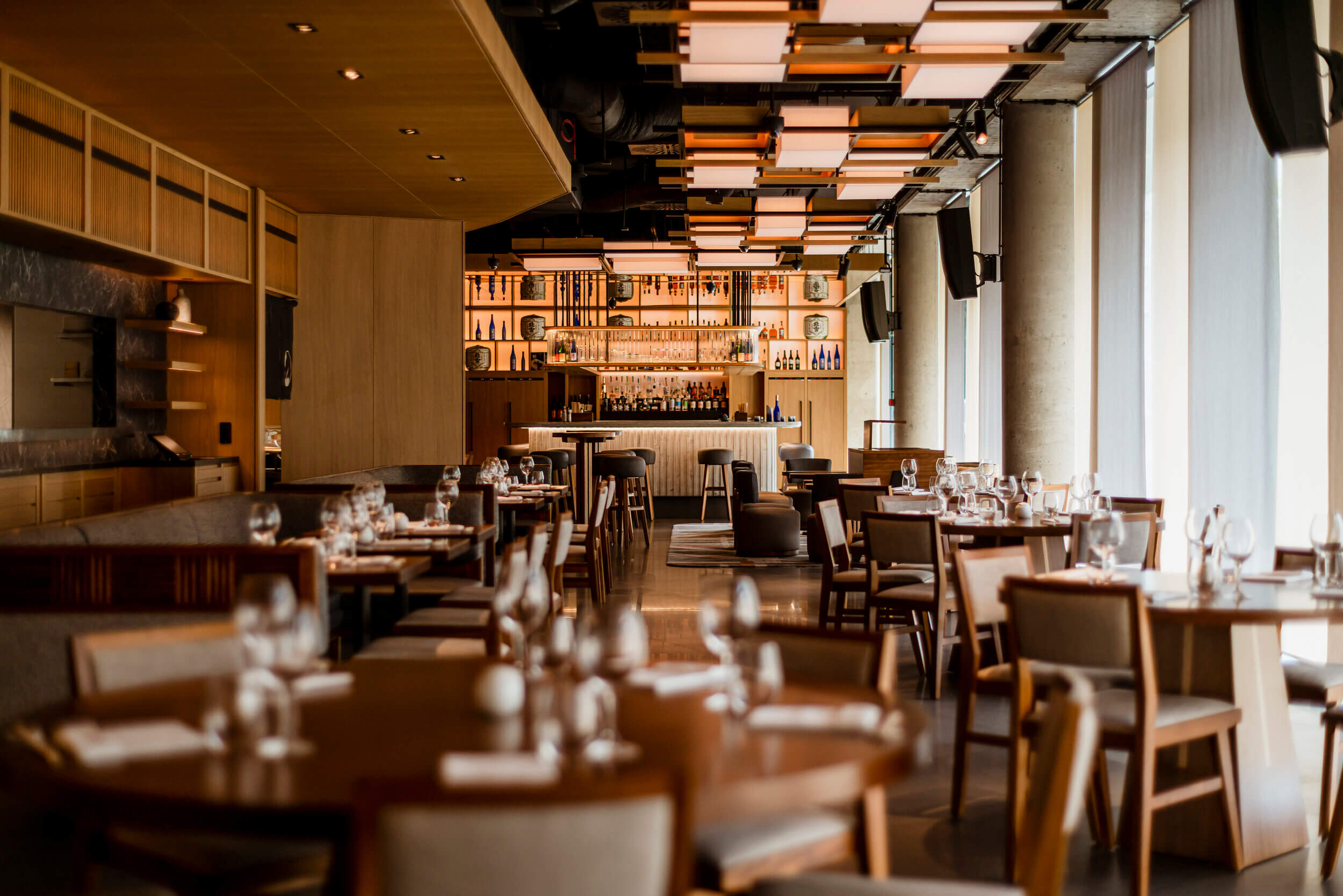 Nobu Warsaw, Poland — Modern luxury restaurant interior with warm wood paneling, geometric ceiling lights, bar seating, and contemporary furnishings bathed in golden ambient lighting.