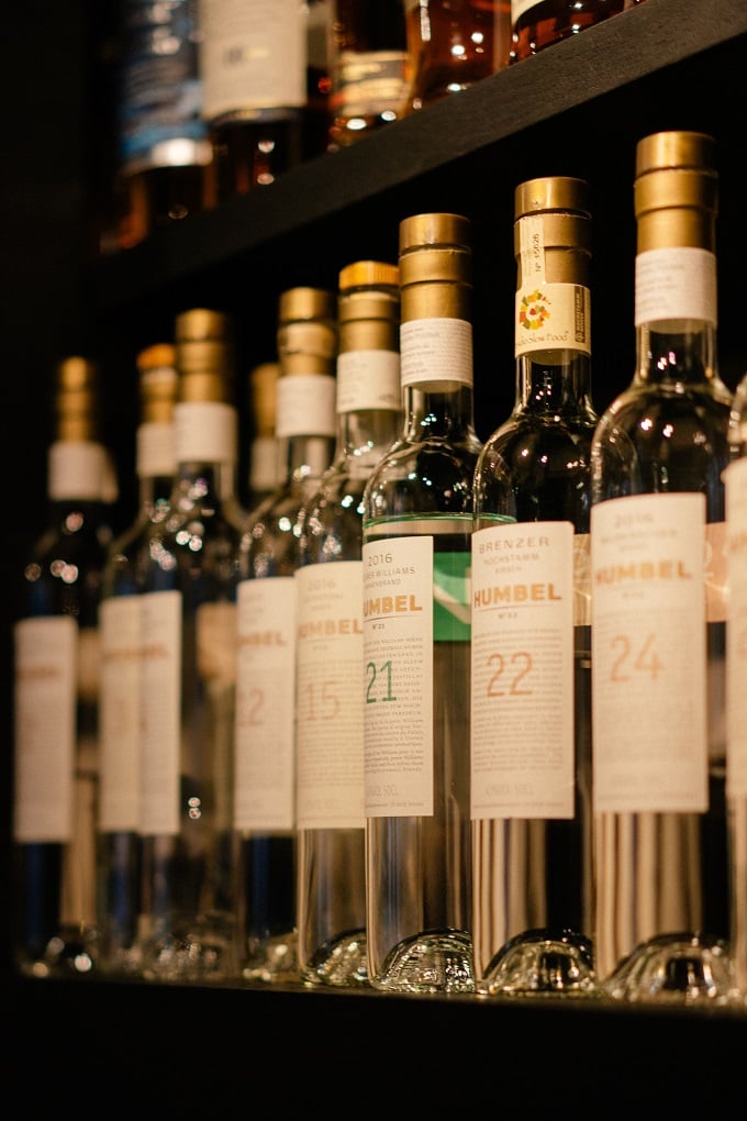 The Library, Europe — Numbered wine bottles displayed on dark shelving with warm ambient lighting and gold foil caps, curated collection aesthetic.