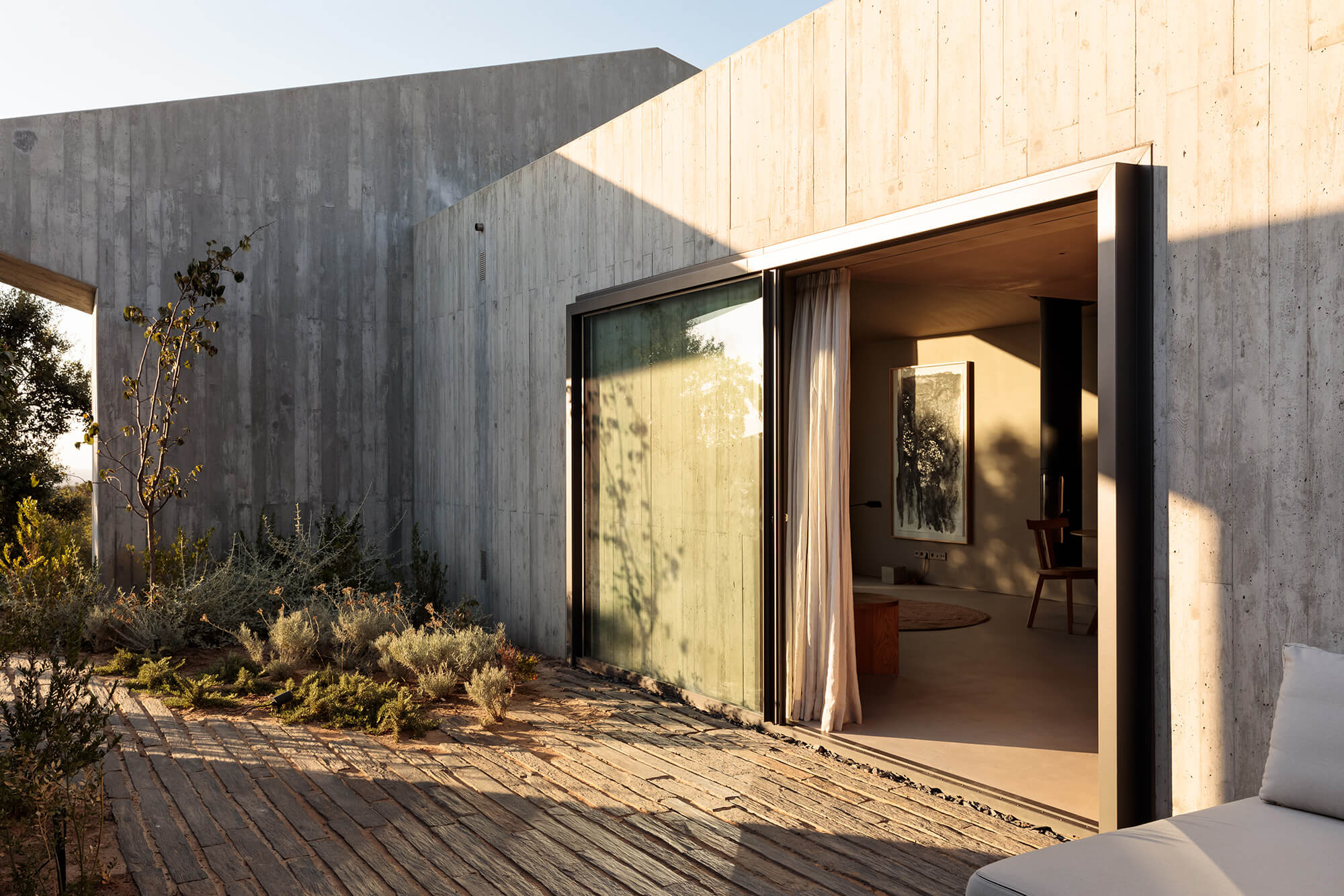Pa.te.os, Europe — Concrete courtyard with sliding glass doors, warm natural light, minimalist landscaping, and wooden deck flooring at luxury hotel.