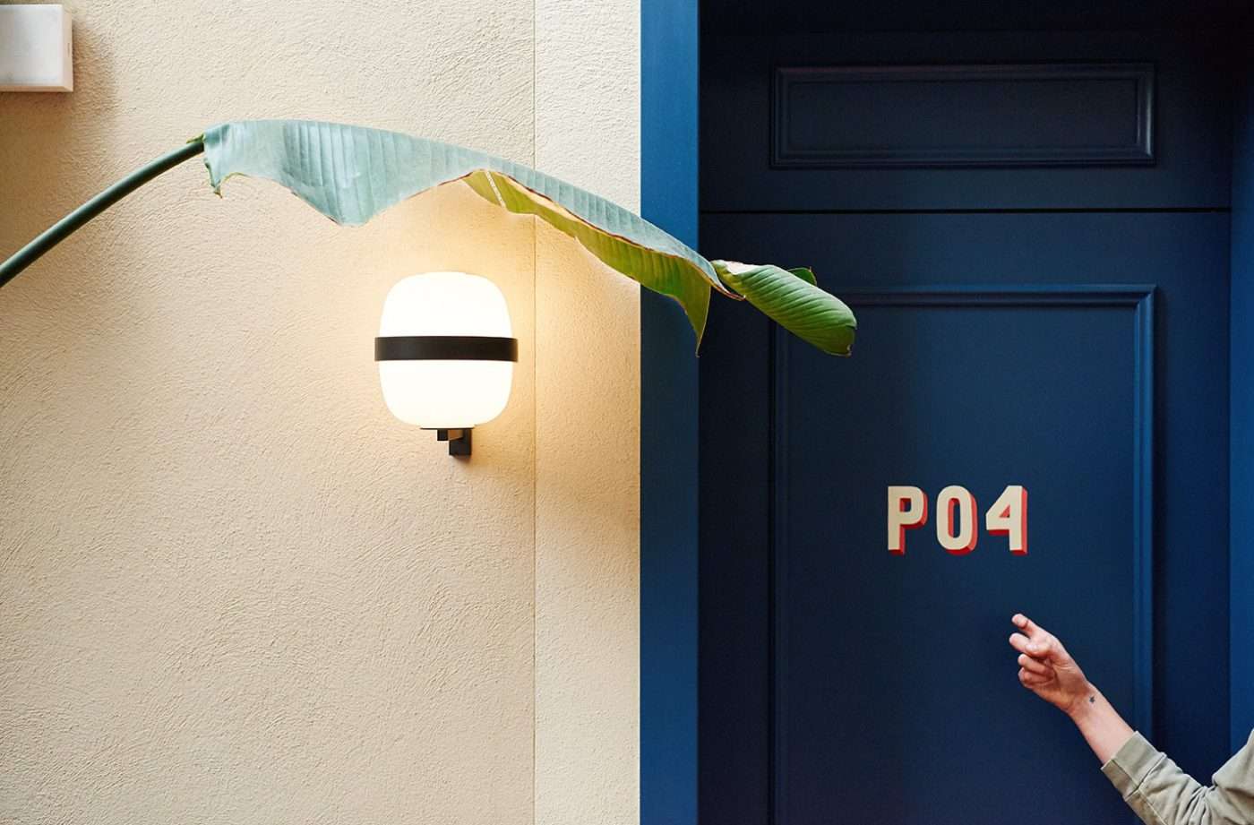 Casa Bonay, Europe — Modern sconce lighting minimalist dark blue door numbered P04 with tropical plant leaf detail and textured cream wall.