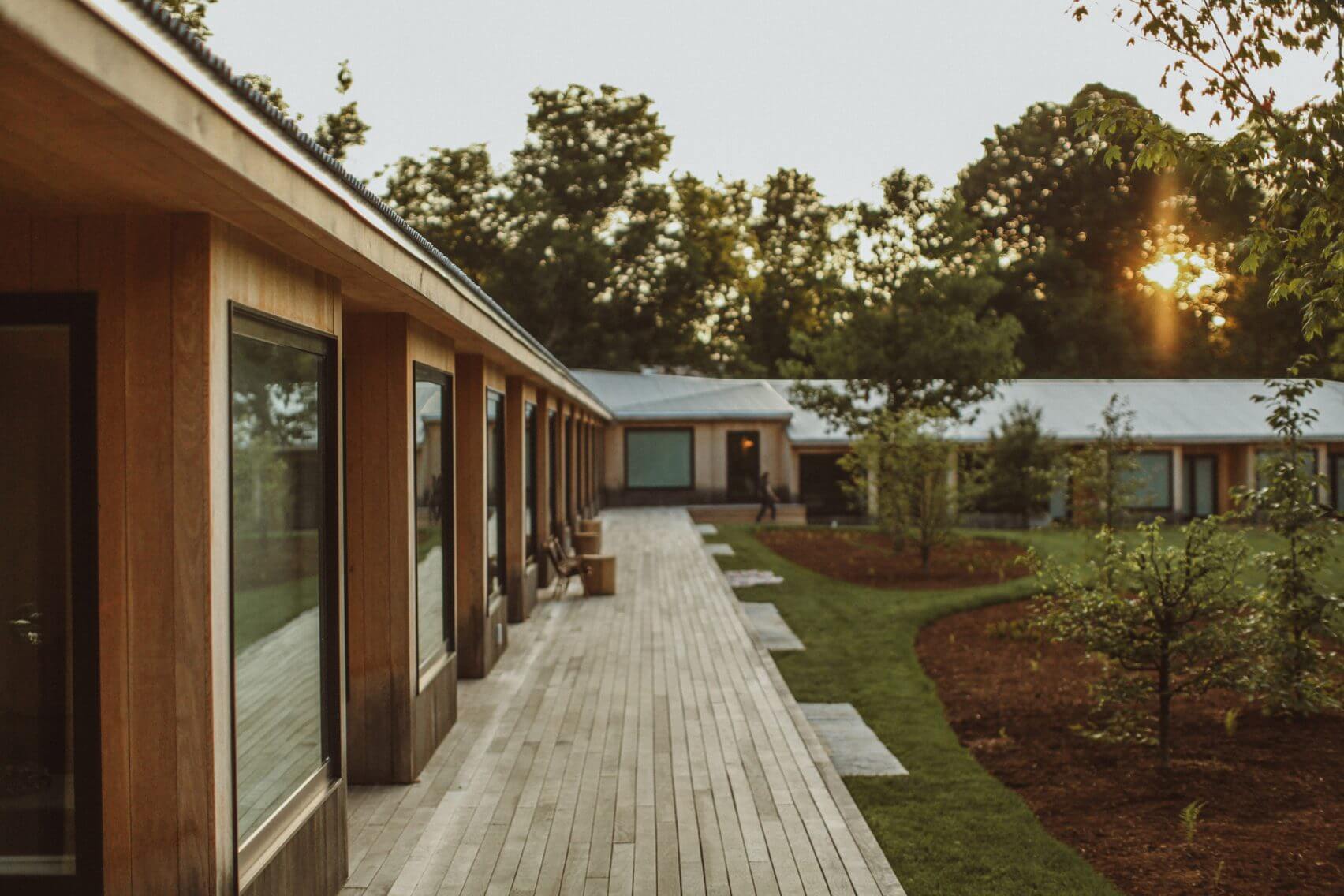 Tourists, North America — Modern timber pavilion with continuous glazing overlooking manicured gardens and tree line at golden hour.
