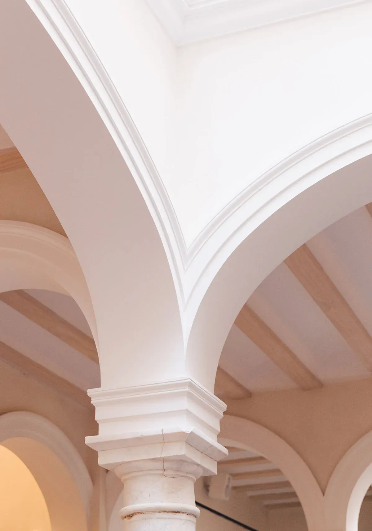 Plácido y Grata, Europe — Arched corridor with white columns and soft peachy walls, minimalist neoclassical architecture with natural light and clean geometric shadows.