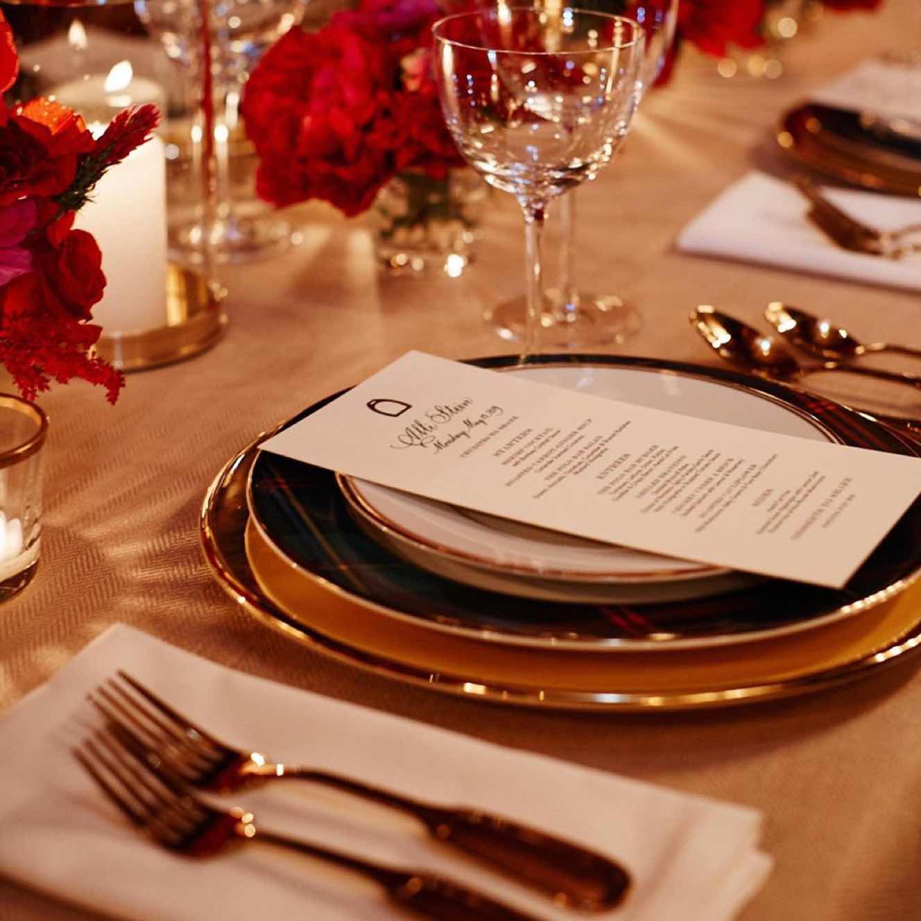 The Polo Bar — Polo Bar, North America — Elegant table setting with gold charger plates, burgundy roses, crystal glassware, and calligraphy menu on warm-toned linens.