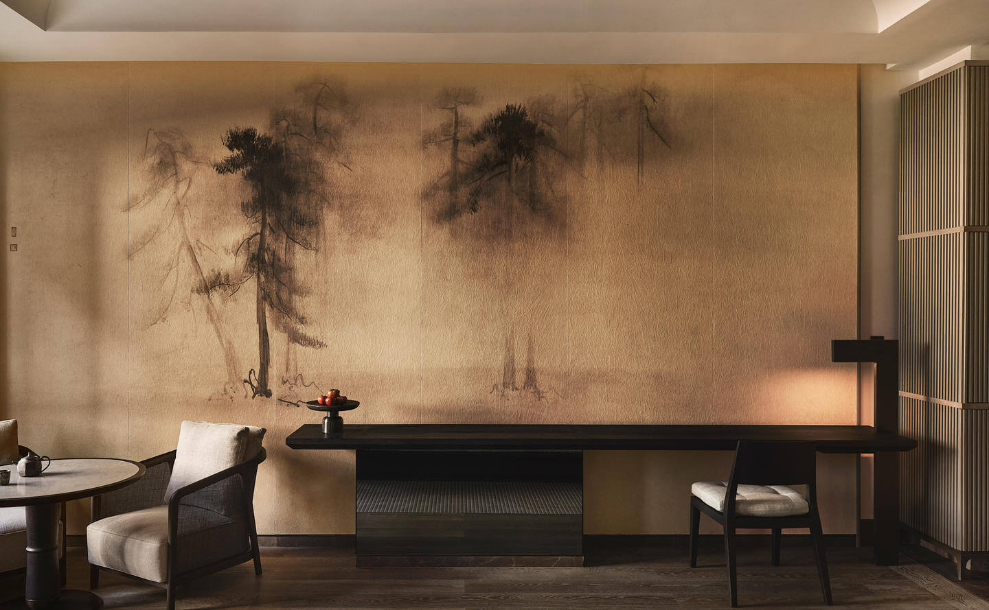 Aman New York, North America — Minimalist lounge with ink-wash mural of pine trees, black furniture, white cushions, warm ambient lighting.