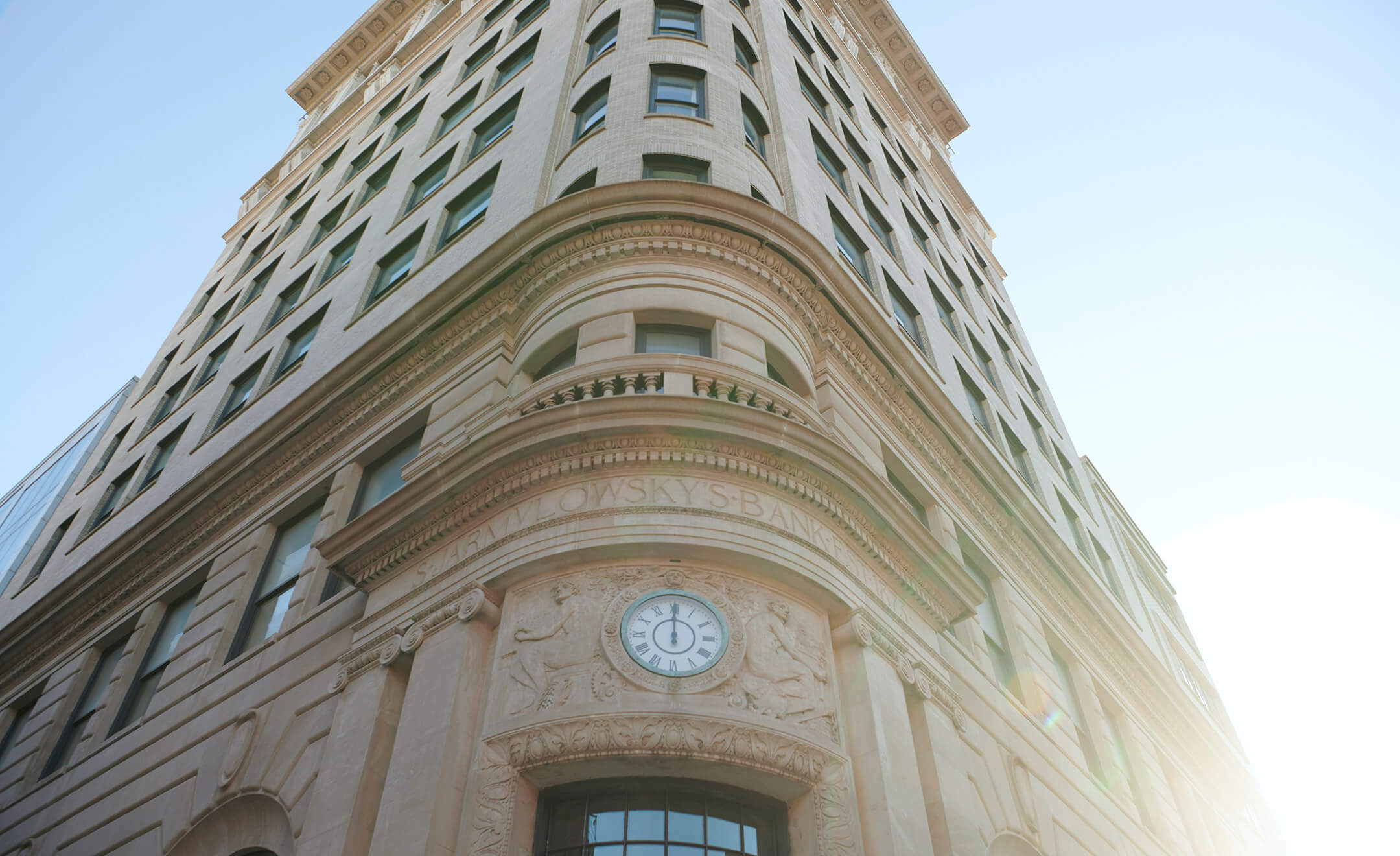 Nine Orchard, North America — Flatiron building corner with curved limestone facade, ornate clock, tall windows, and classical architectural detailing against clear sky.