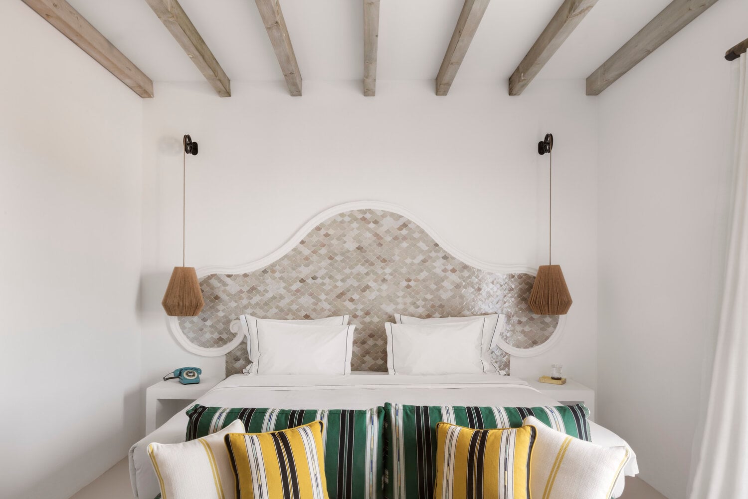 Quinta da Comporta, Europe — Coastal bedroom with curved stone tile headboard, white bedding, striped pillows, exposed beam ceiling, pendant lighting.