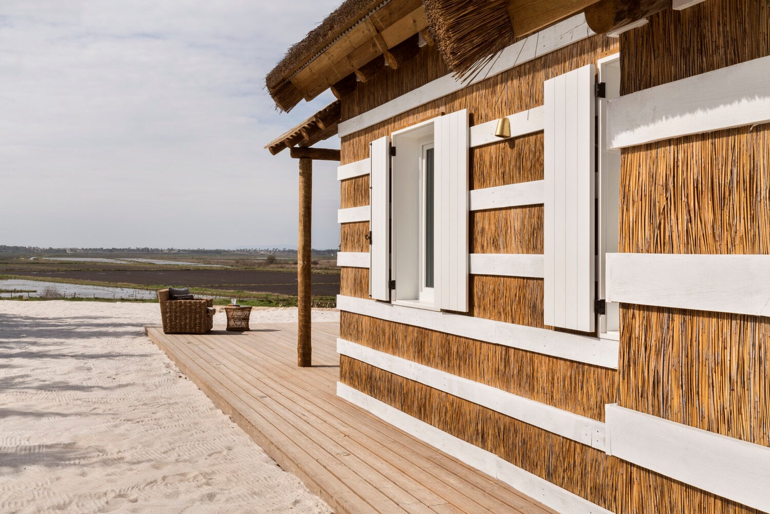 Quinta da Comporta, Europe — Thatched-roof beach pavilion with white and natural reed cladding, wooden deck, lagoon views, contemporary coastal architecture.