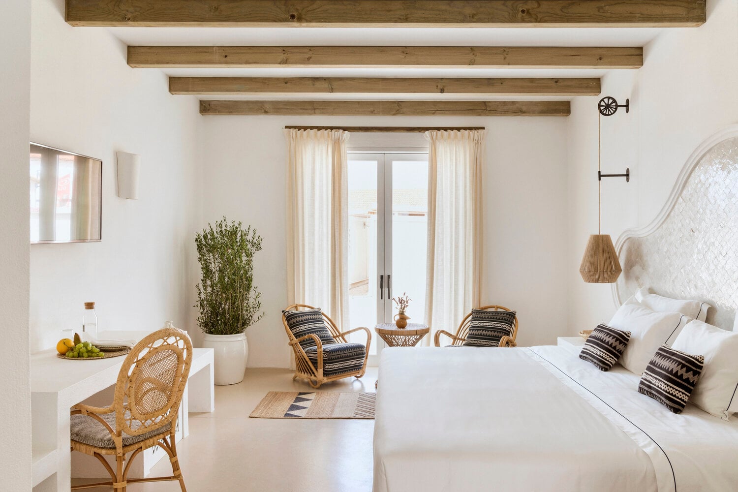 Quinta da Comporta, Europe — Minimalist bedroom with exposed wooden beams, white walls, rattan chairs, cream linen bed, and French doors opening to coastal views.